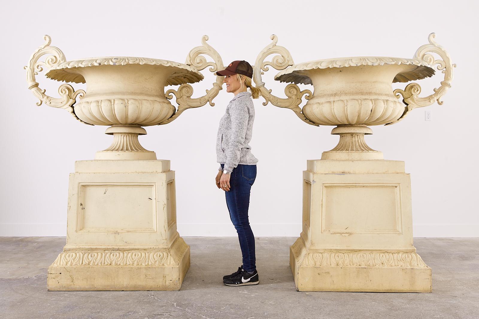 Impressive pair of monumental palace sized metal garden urn planters or jardinaires. Standing over 6 feet tall and made in the French neoclassical style with scrolled acanthus handles on each side. Permanently mounted on large square pedestals with