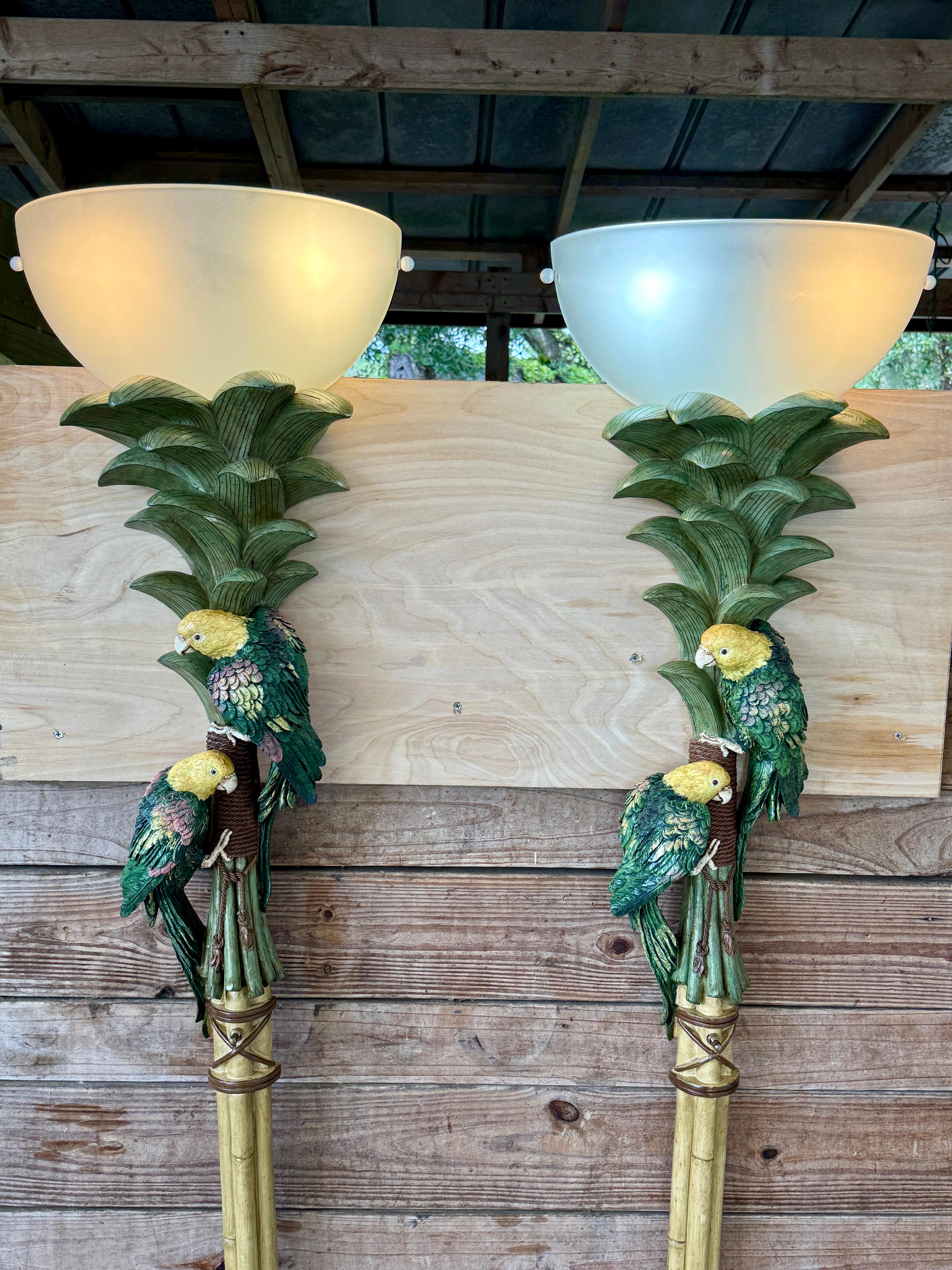 A sculptural pair of Coastal Tropical parrot torchiere wall lights by Pacific Coast Lighting, dated 2003. Monumental in scale and design, these cast resin wall sconces feature lush palm fronds and a trio of vibrant green and yellow parrots perched