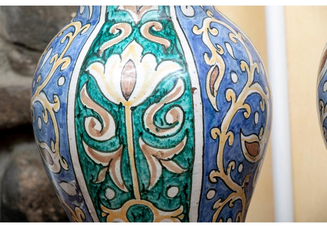 Vases à couvercle en poterie de forme bulbeuse se rétrécissant à la base. Décorée de bandes bleues et turquoises avec des vignes enroulées et des fleurs à longues tiges jaunes, blanches et brunes. Avec des couvercles hauts