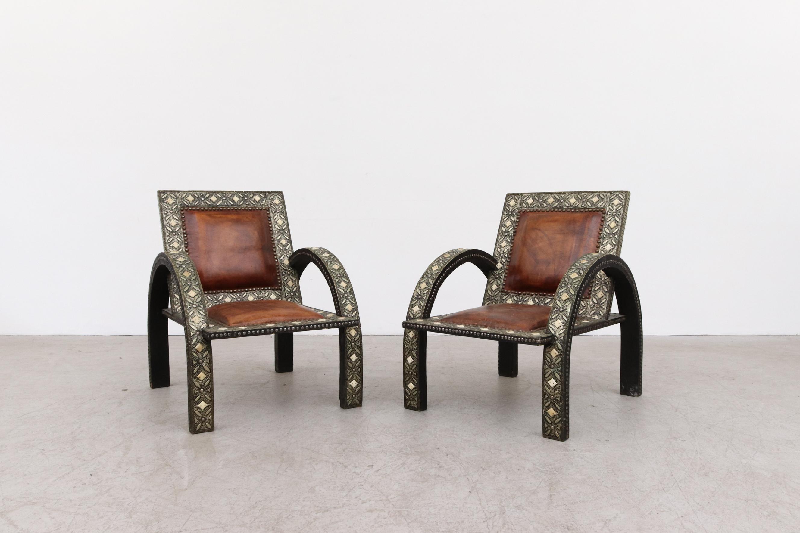 Pair of Moroccan-meets-mid-century lounge chairs with leather seating and decorative frames. 
A unique piece of home decor. Seat depth is 19.5'. In original condition with wear consistent with their age and use. Set Price.