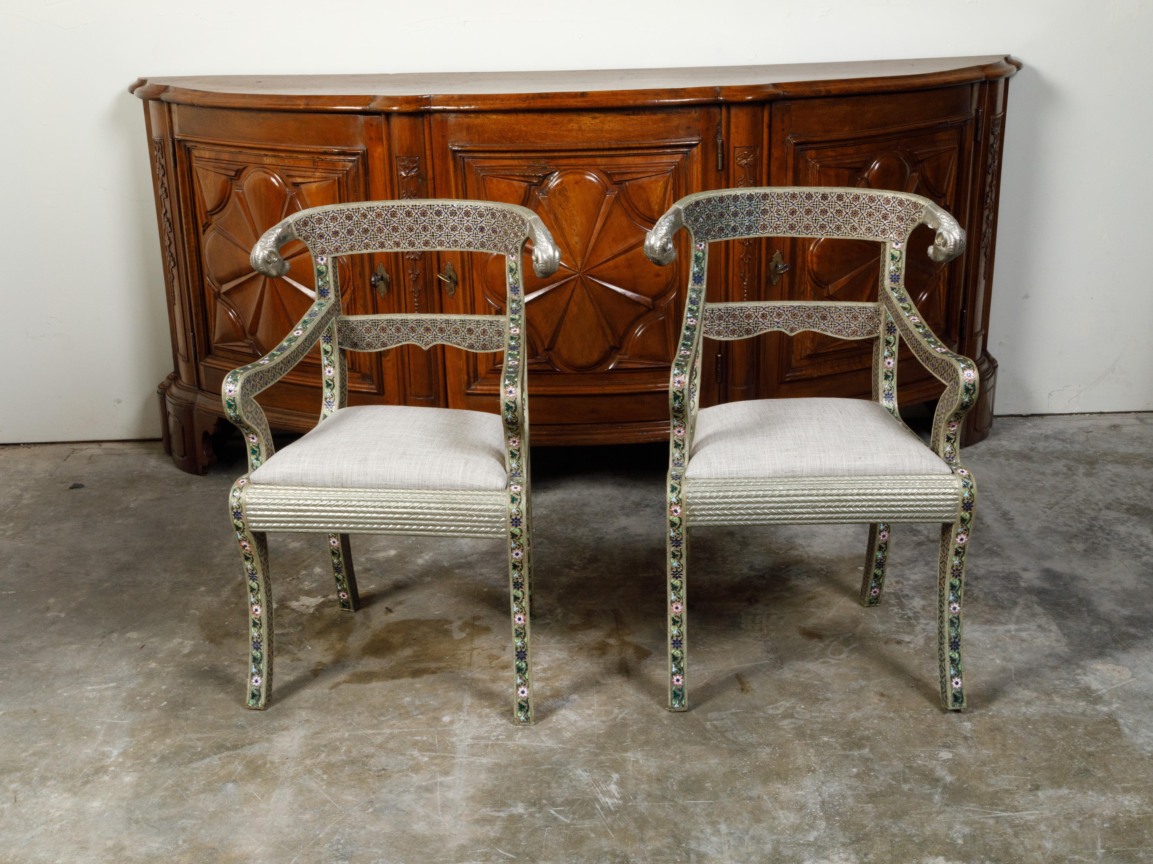 A pair of Moroccan metal armchairs from the mid 20th century, with enamel décor and rams' heads. Created in Morocco during the second quarter of the 20th century, each of this pair of armchairs features a pierced back with curving rail and rams'