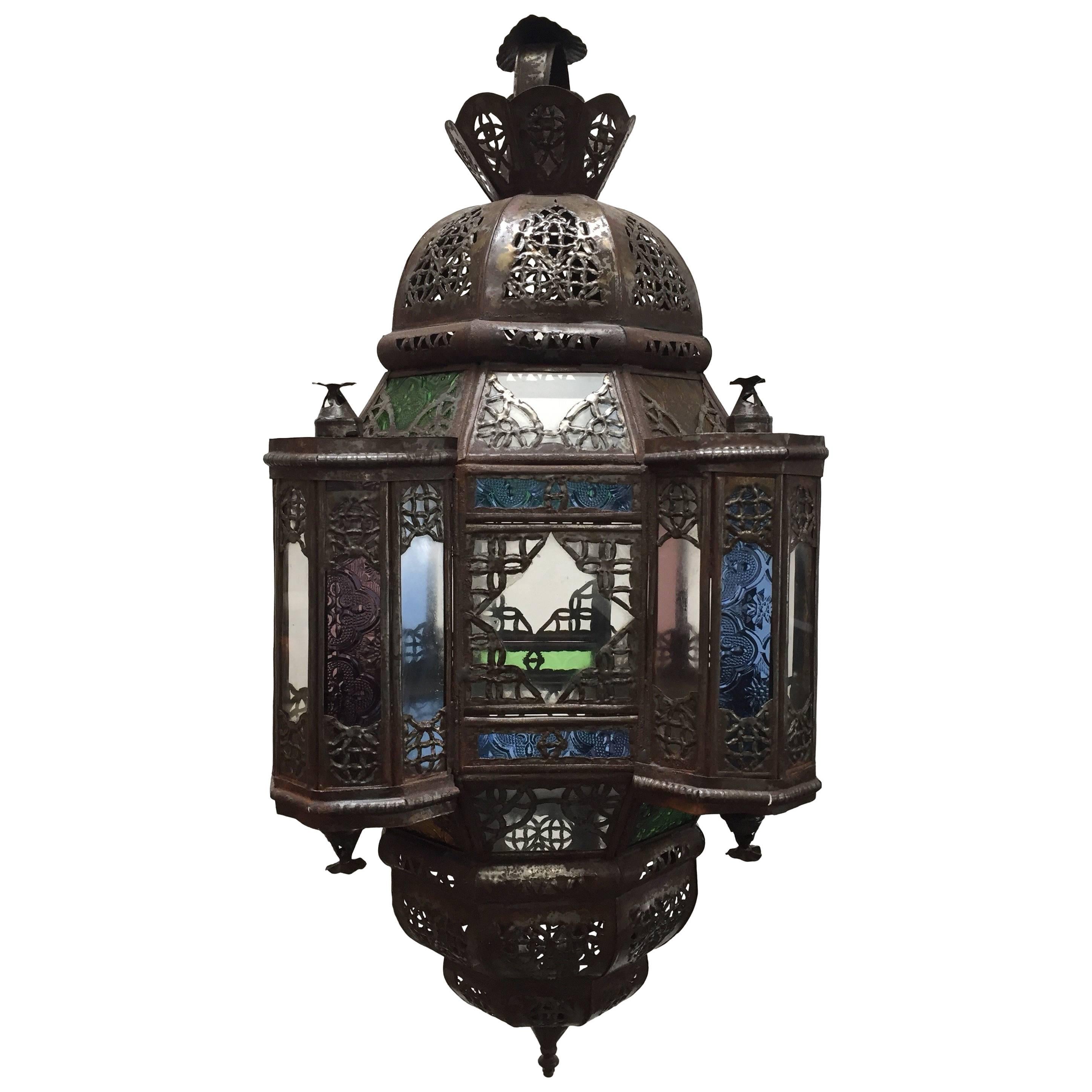 Pair of handcrafted Moroccan glass pendant with clear and colored glass, square shape with towers and a dome with metal filigree.
This multi-color Moroccan glass lantern with Moorish arches in metal filigree and colored glass in green, blue,