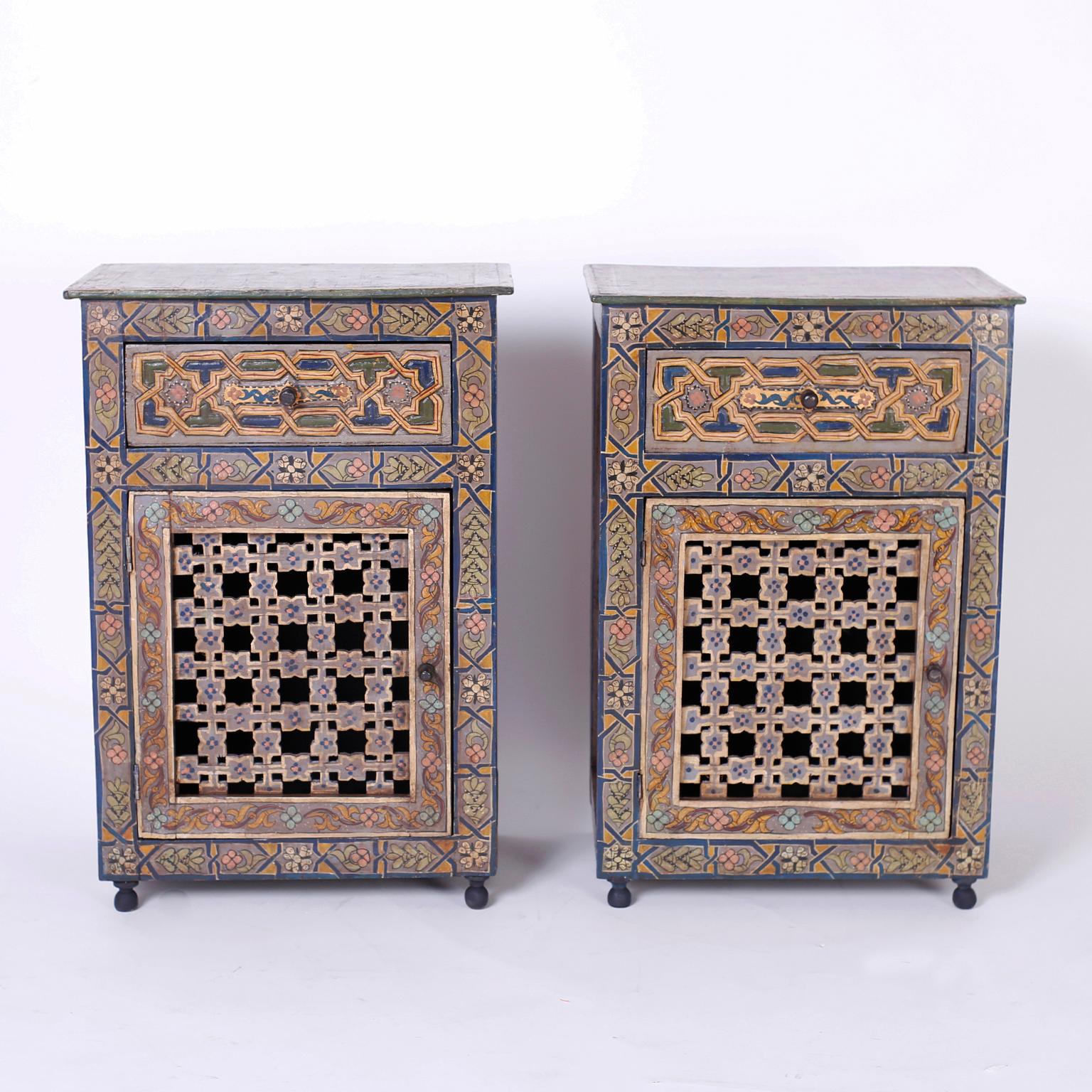 Pair of antique Moroccan stands decorated in a rustic folky style depicting Classic geometric and floral designs. Featuring one drawer over an open fretwork cabinet door and turned ball feet.
   
