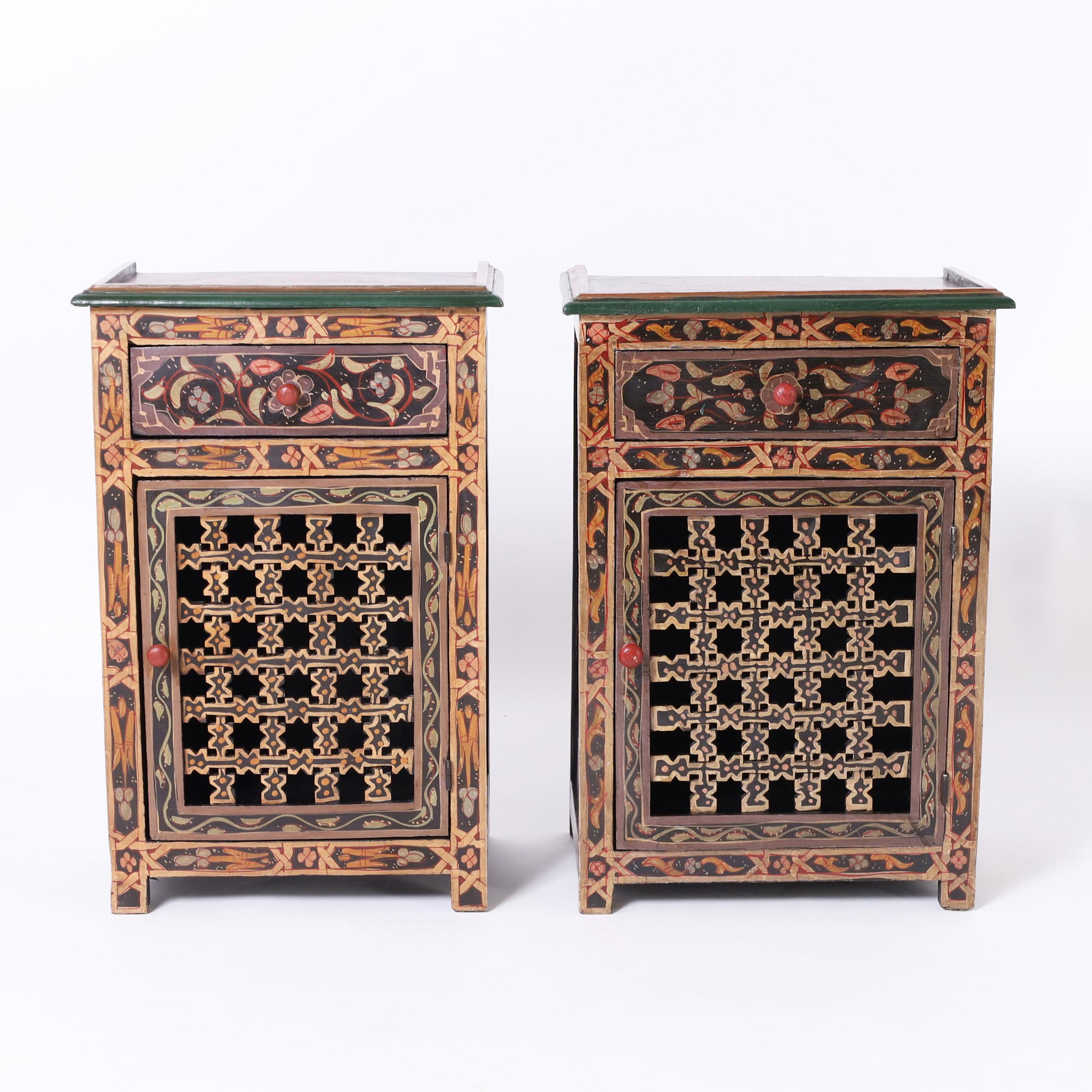 Enchanting pair of vintage Moroccan stands crafted in indigenous hardwoods with one drawer over a cabinet door with open fretwork and paint decorated in floral designs with distinctive mediterranean colors.