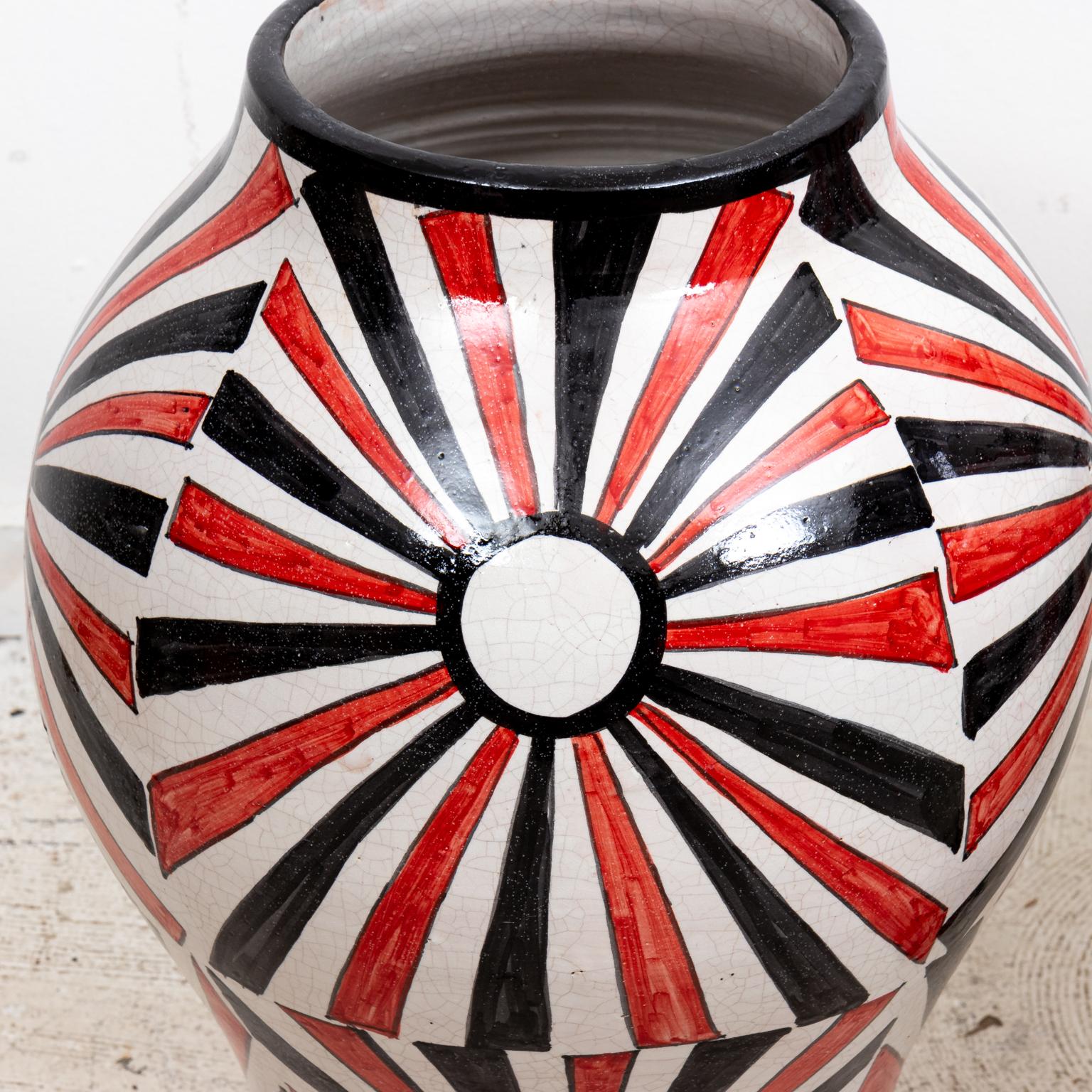 Pair of Moroccan jars with dome shaped lids. The jars are painted in a red and black sunburst pattern on a white background. Please note of wear consistent with age including paint loss, chips, patina, and finish loss.