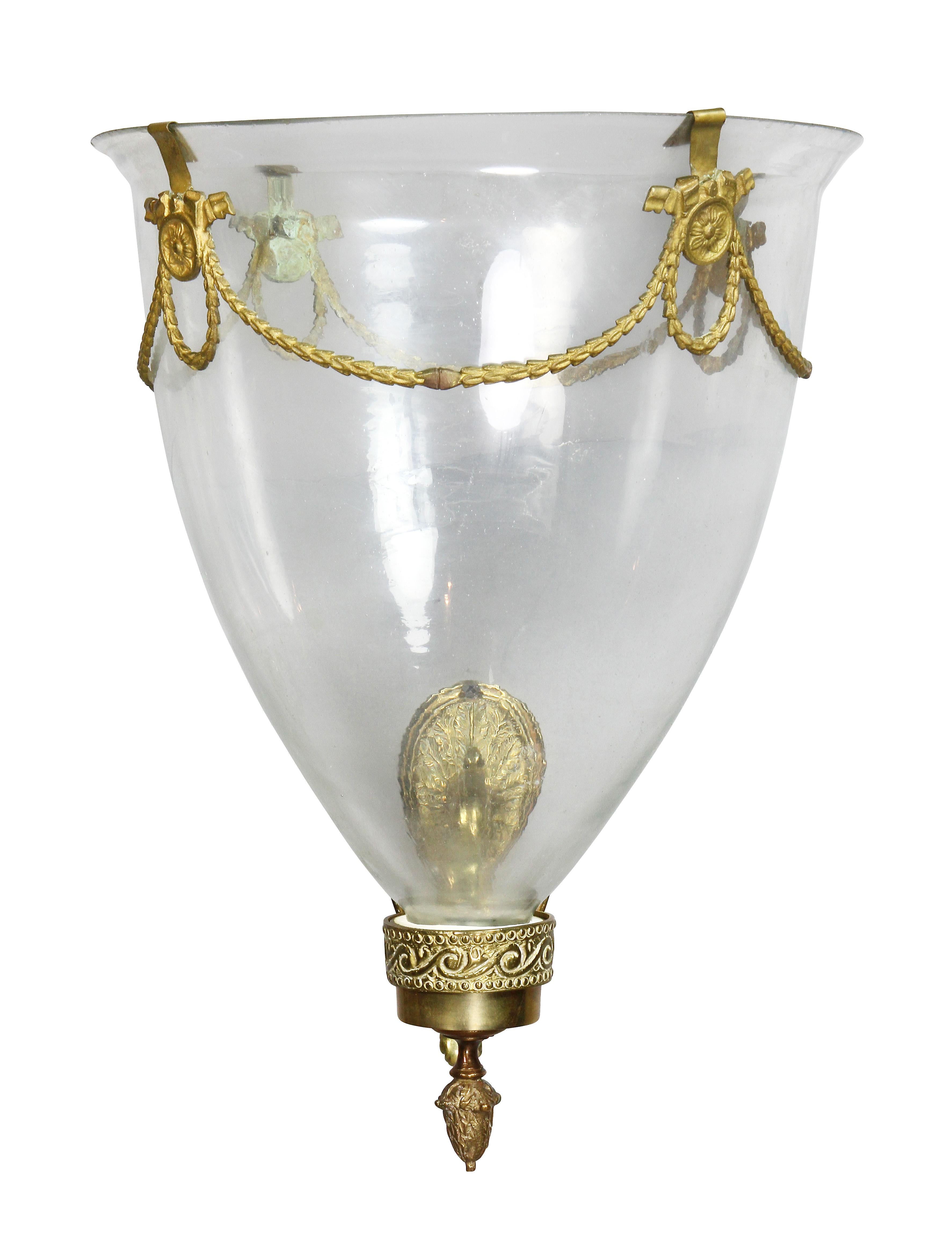 Conical with gilt metal swags, the shade with brass collar that fits tightly into the brass holder, scroll form wall bracket. One shade has a chip at top. William Hodgins Estate.