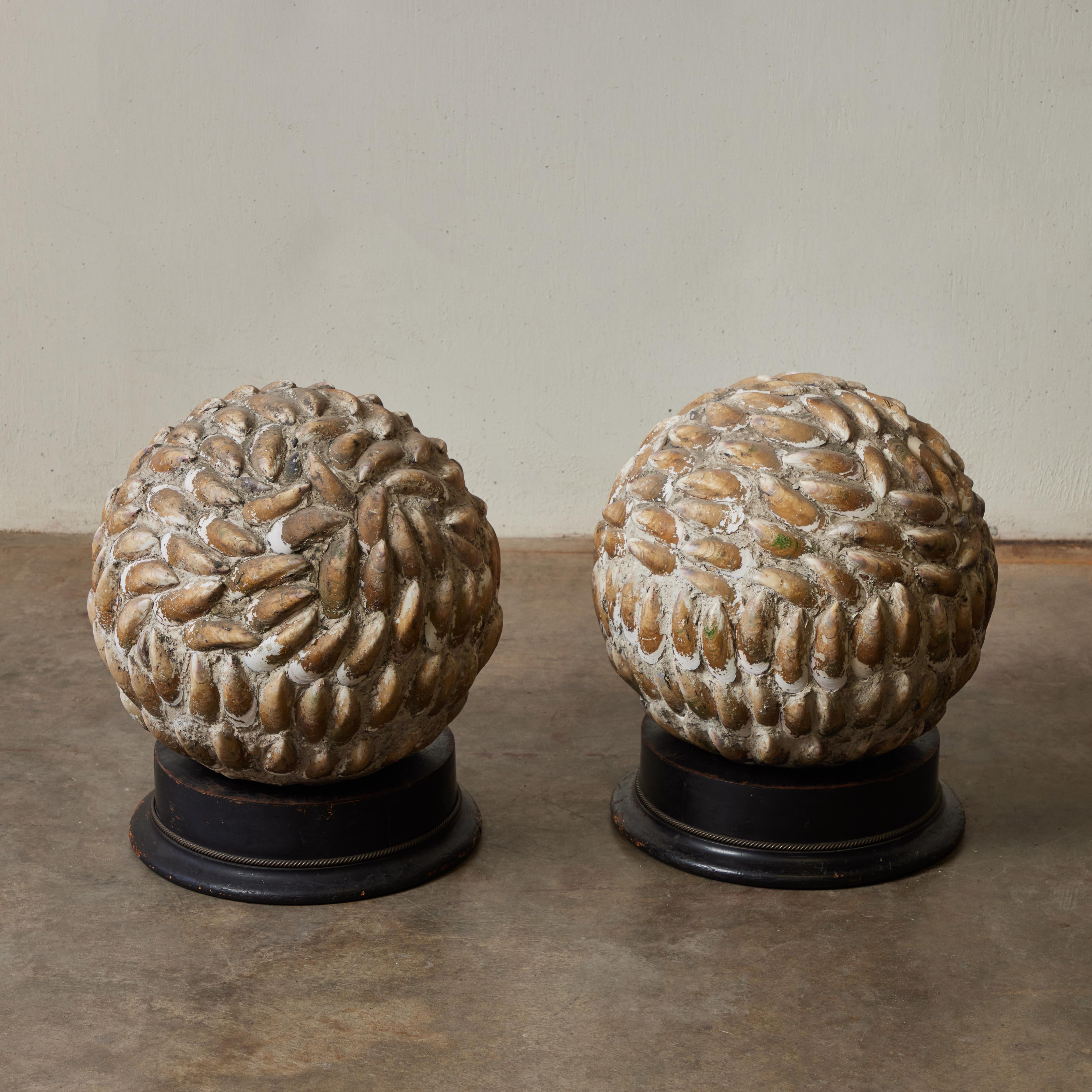 Paire de magnifiques sculptures en forme de sphère provenant de l'Angleterre des années 1920. Avec un motif rythmique de coquilles de moules et montés sur des socles ronds en ébène, la paire ajoute une touche naturaliste à une table ou une étagère.