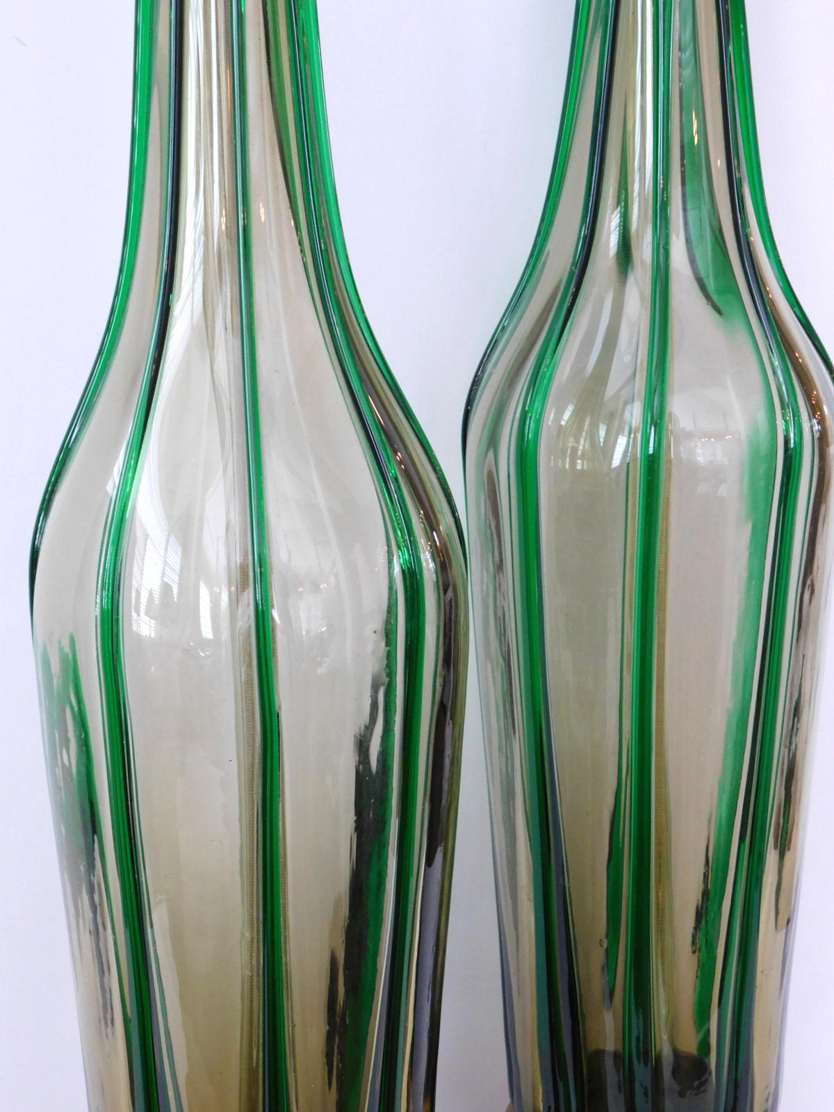 Each tall, slender ovoid-form glass lamp decorated with applied green vertical strands, raised on a gold and ebonized painted metal base, measures: height 21.75