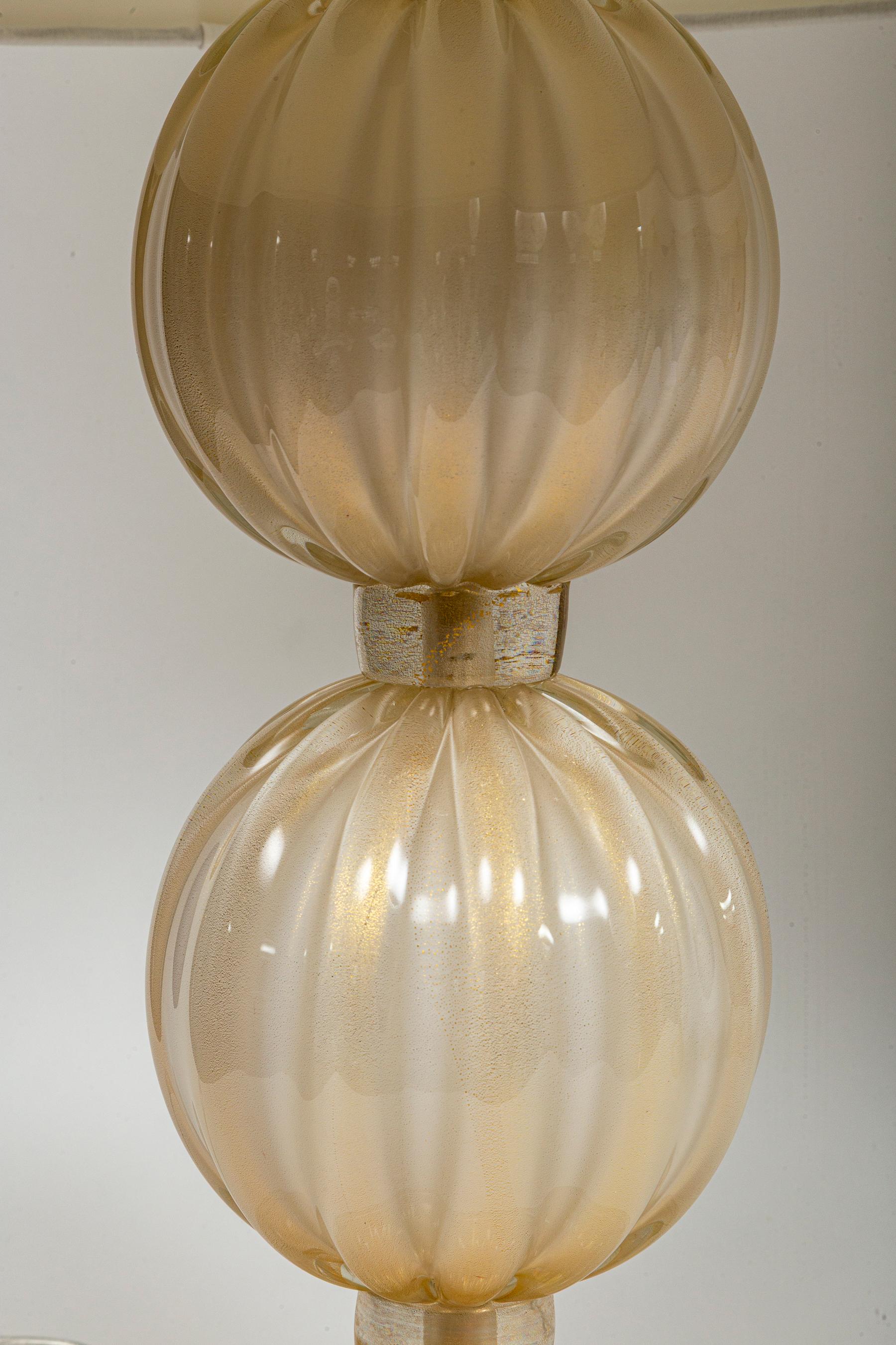 Lovely pair of lamps comprised of  large  23k gold blown reeded balls finishing with an elegant dome shaped base.

Illuminated with E26 bulb with warm LED bulbs.

Origin: Murano, Italy

Dimensions Of Glass: 10″ diameter, 16″ high to the top of the