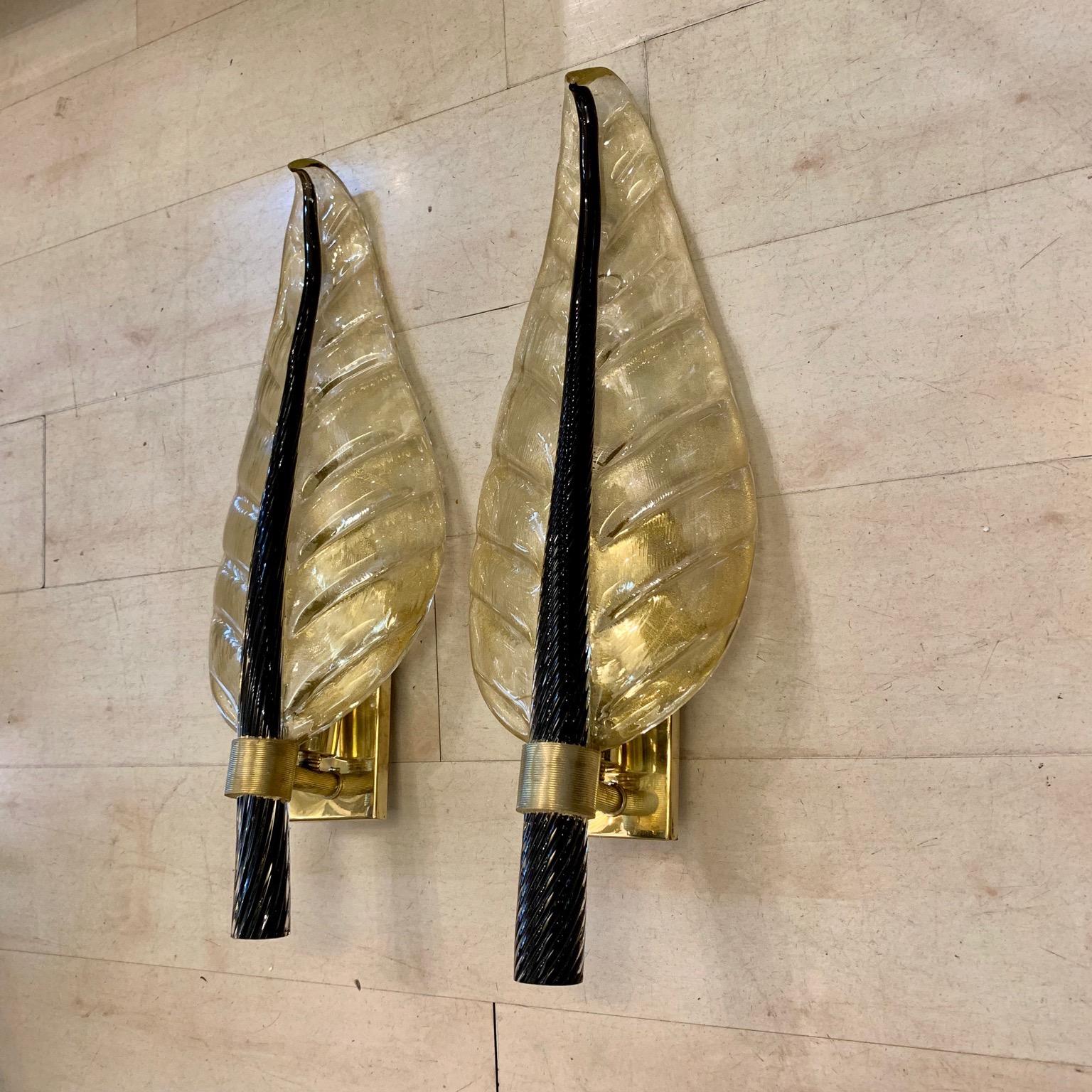 Pair of Murano glass gold leaf sconces with black torchon glass leaf stem, brass structure, one bulb for lamp.
These sconces are in Murano hand blown thick glass with gold flecks, the stem of the leaf is in full black torchon Murano glass.