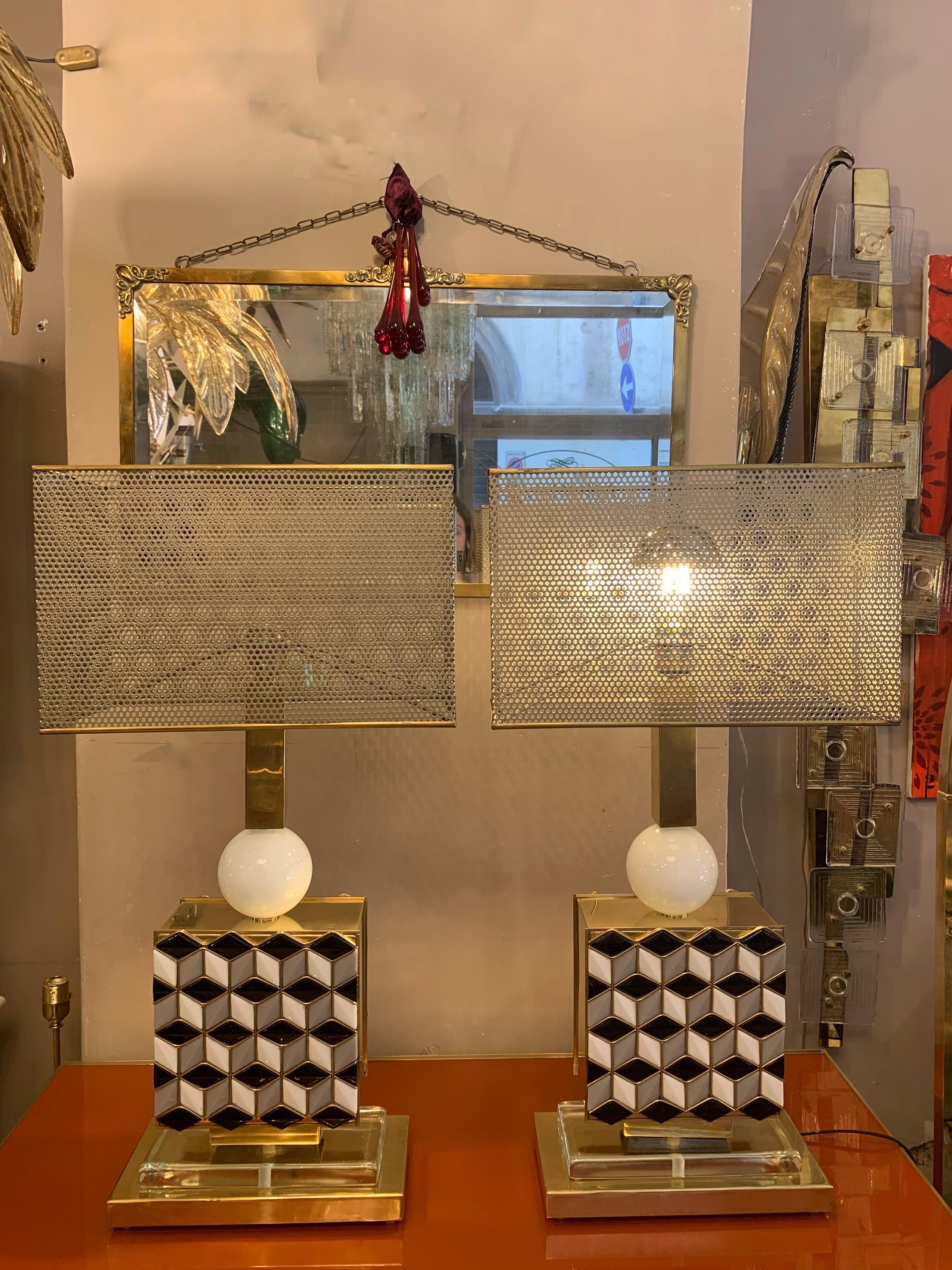 Pair of table lamps in black, white and grey Murano glass mosaic with inlays and brass structure. The lamps are presented with rectangular perforated lampshades with golden metal profile. 
One light bulb each lamp.
Measures of the lampshade: cm 40 x