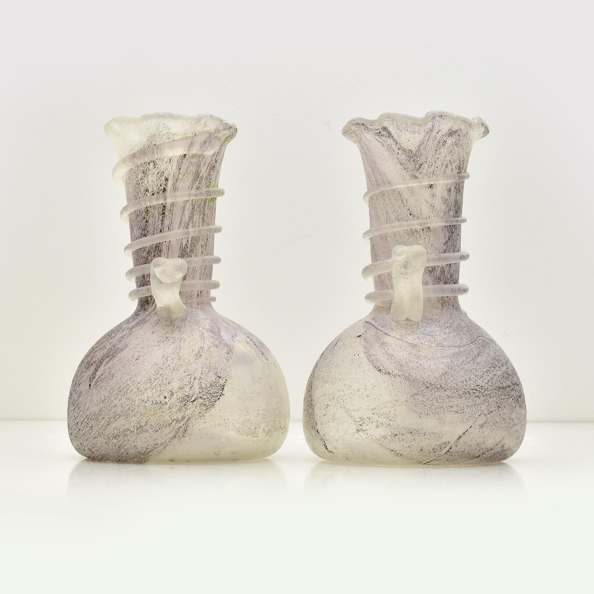 Questa elegante coppia di vasi in vetro di Murano sfoggia la rinomata tecnica Scavo, che conferisce loro un aspetto antico e romano. Realizzato da abili artigiani italiani, la superficie di ogni vaso è trattata con cura per ottenere una finitura