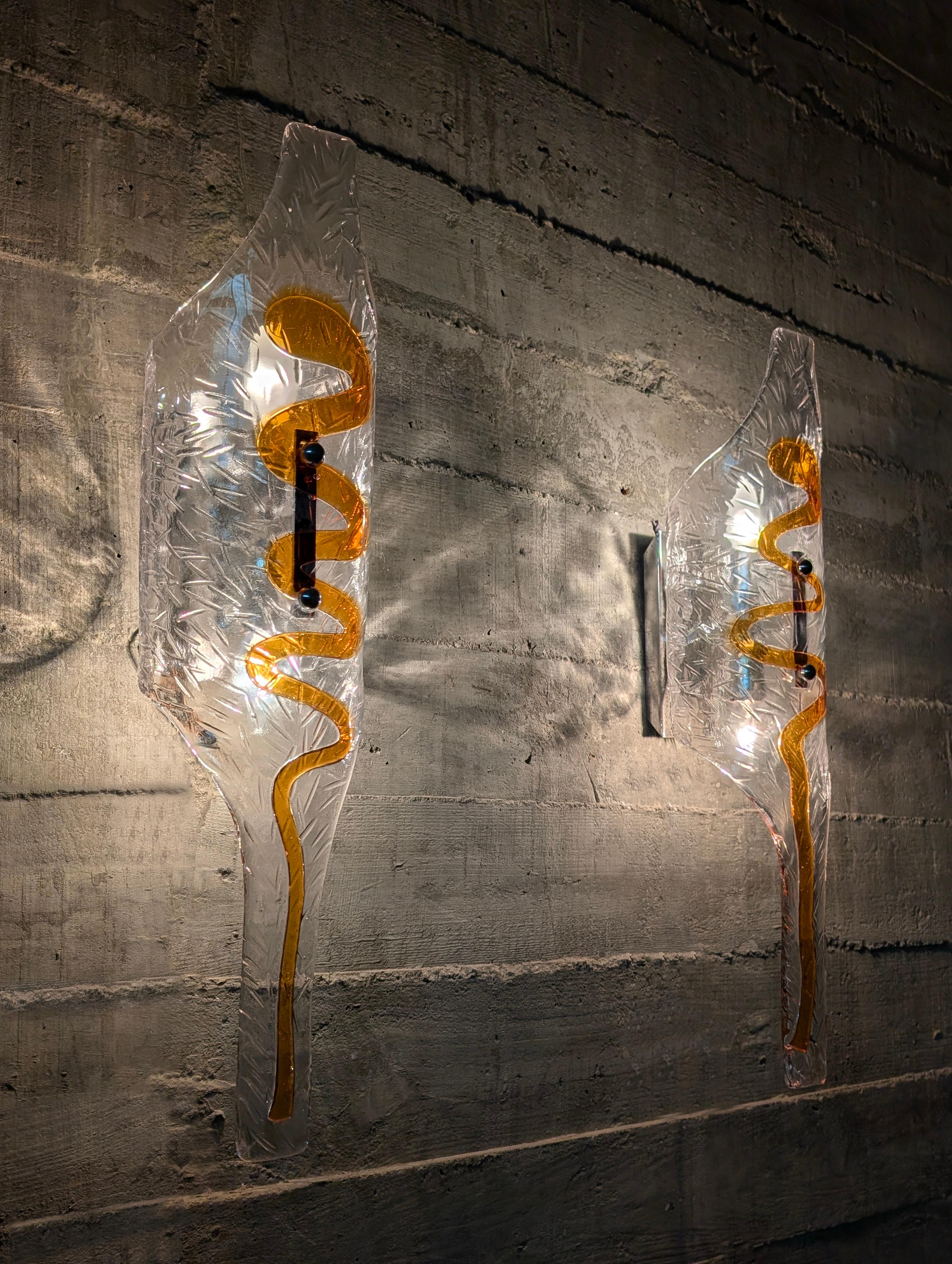 Realizzate con la maestria del vetro di Murano, questa imponente coppia di appliques italiane degli anni '70, attribuite ai disegni di Toni Zuccheri per Mazzega, incarnano la fusione tra sperimentazione artistica e raffinatezza luminosa. I pezzi