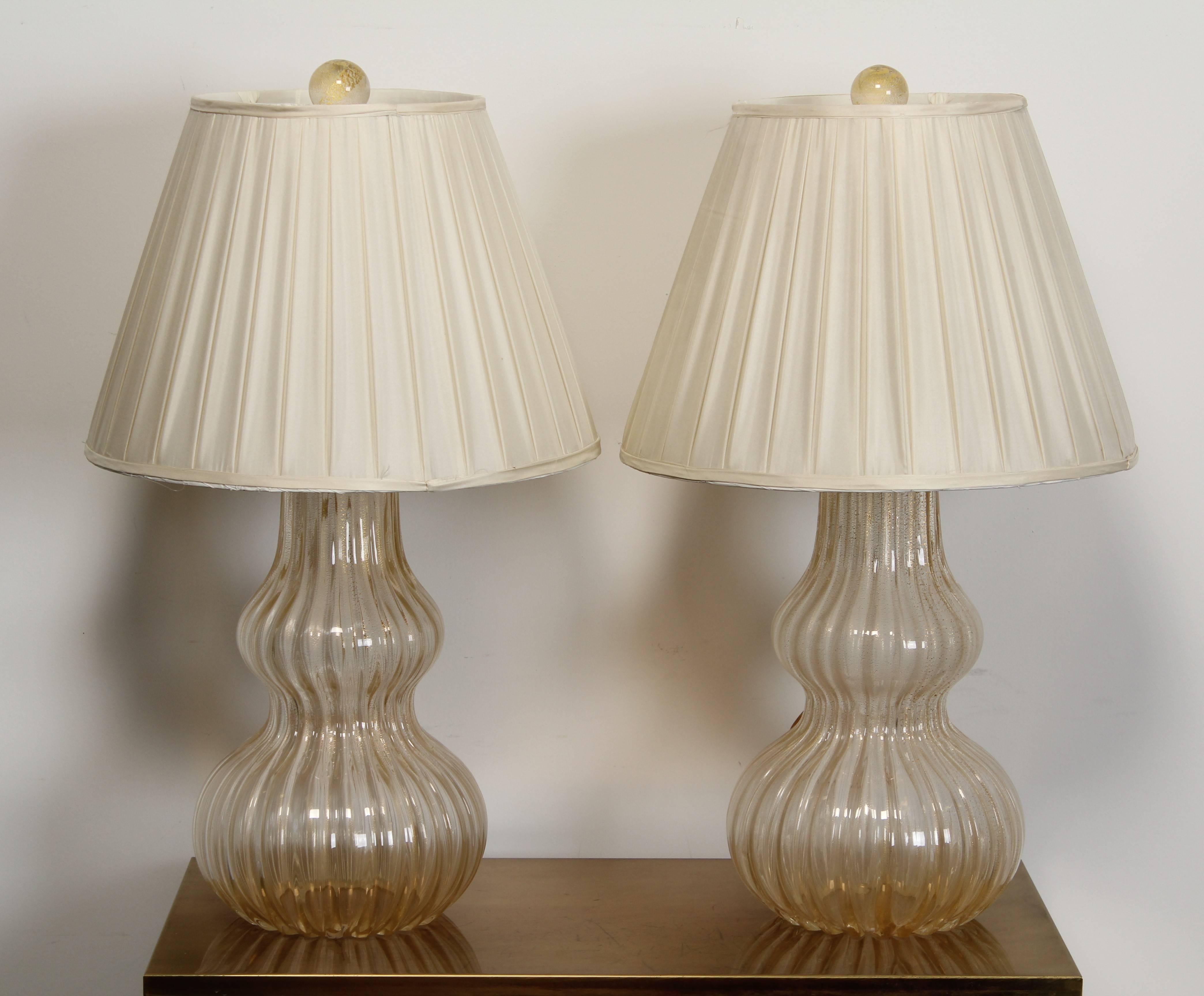 An elegant pair of Murano glass table lamps, 1980. The lamps have gold flecking to surface with round glass finials. Shades included.