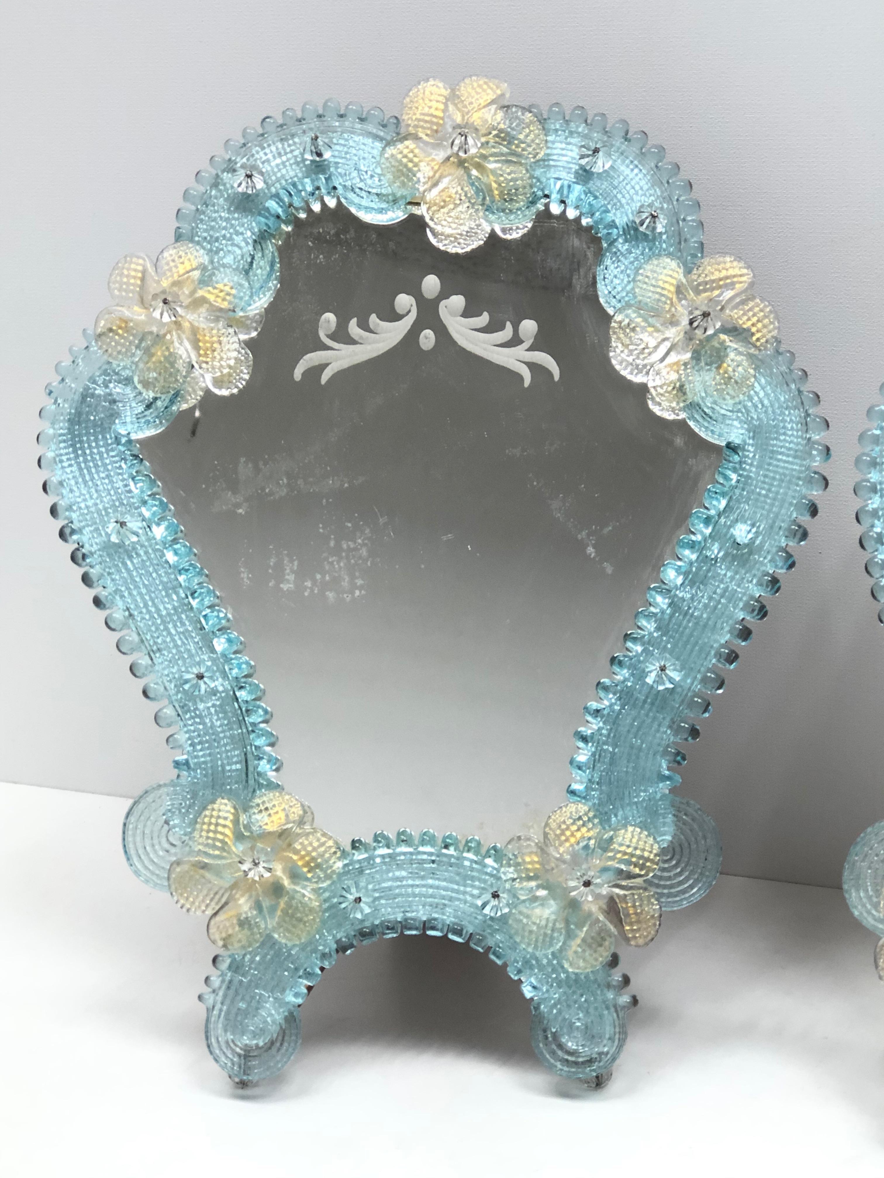 A pair gorgeous Murano glass vanity mirrors surrounded with handmade light blue glass parts and clear and golden colored flowers. Can be used as a table or a wall mirror. With minor signs of wear as expected with age and use. A nice addition to any