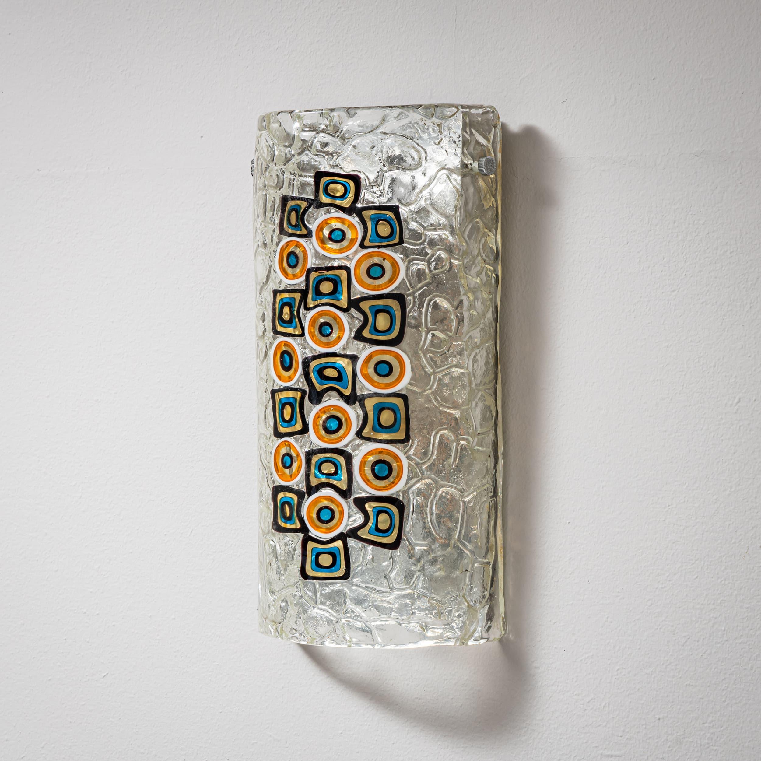 Dos apliques decorativos de cristal de Murano con inclusiones de colores y textura de cristal de hielo. La superficie irregular crea un vibrante juego de luces. Montados en placas metálicas.