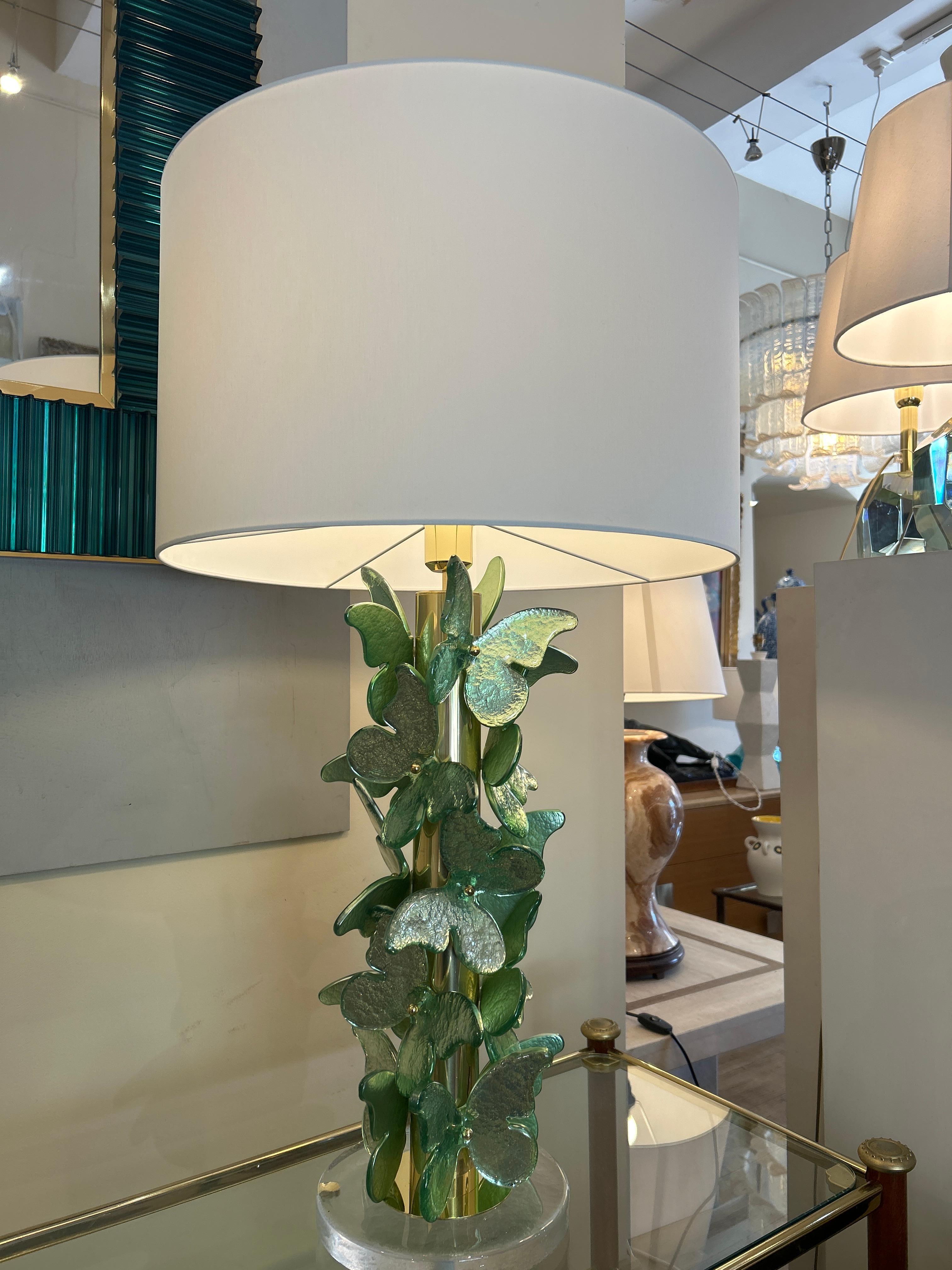 Paire de lampes Murano sont des pièces décoratives élégantes avec un style botanique et sophistiqué. Il repose sur une base circulaire en verre transparent, ce qui lui confère un effet de légèreté et de modernité. La base de la lampe est décorée