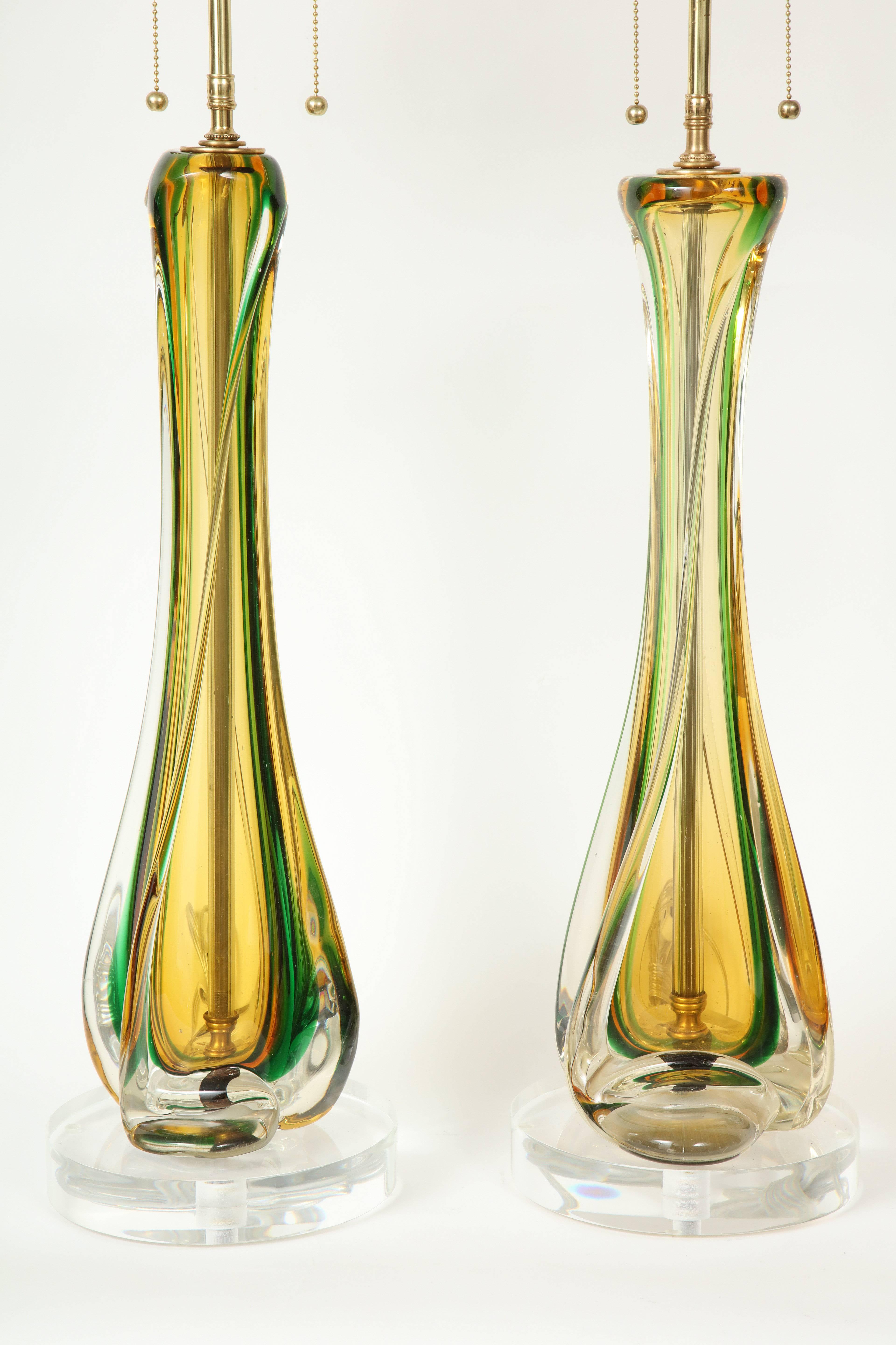 Large pair of Murano lamps by Seguso.
This handblown pair of Sommerso glass lamps in shades of green and amber encased a clear body are mounted on thick Lucite bases. 
They are newly rewired with polished brass double clusters that take standard