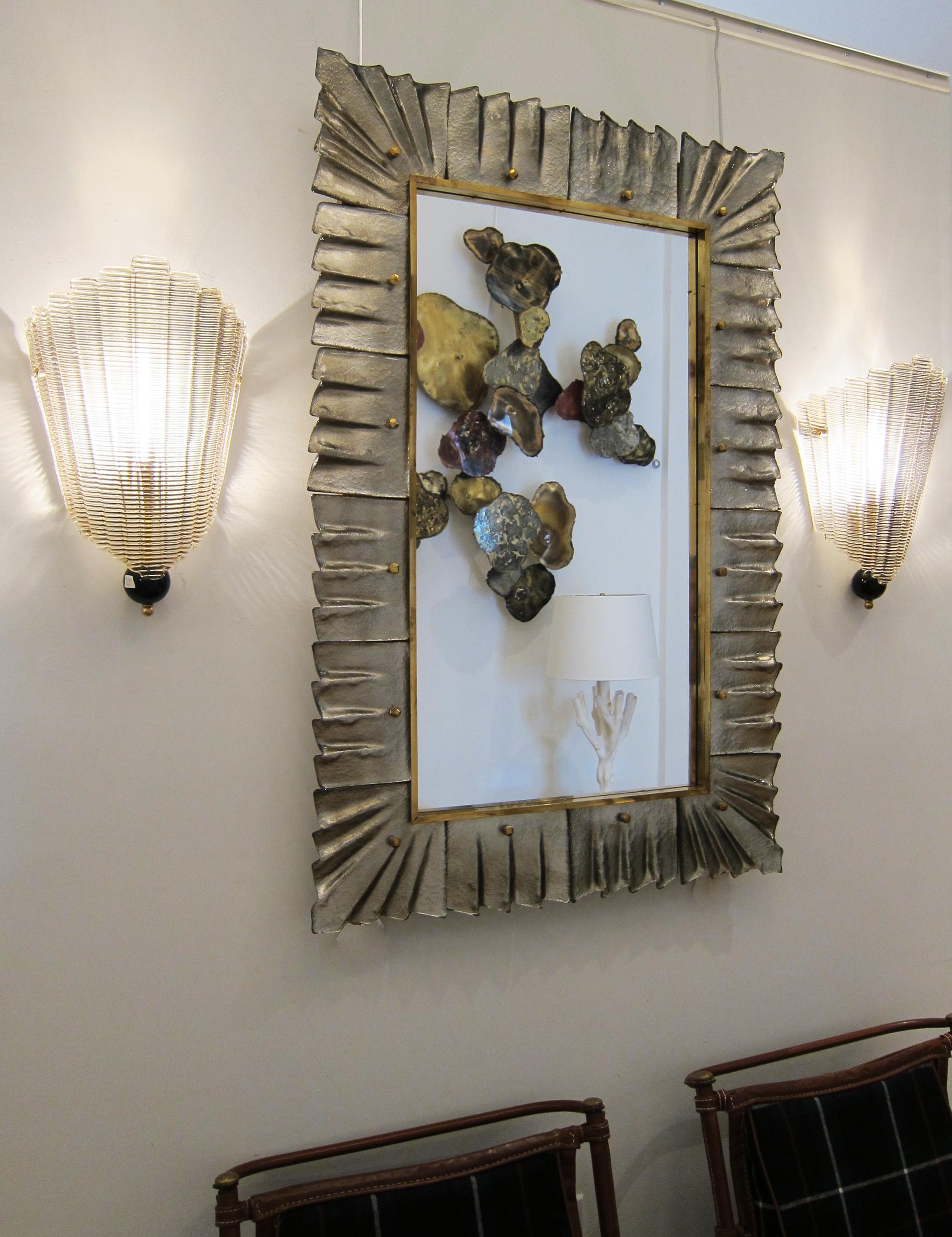 Pair of contemporary Murano silver glass framed mirror, in stock
Rectangular mirror plate surrounded with undulating glass tiles in silver color held by brass cabochons.
Luxury handcrafted by a team of artisans in Venice, Italy.
Can be easily hung