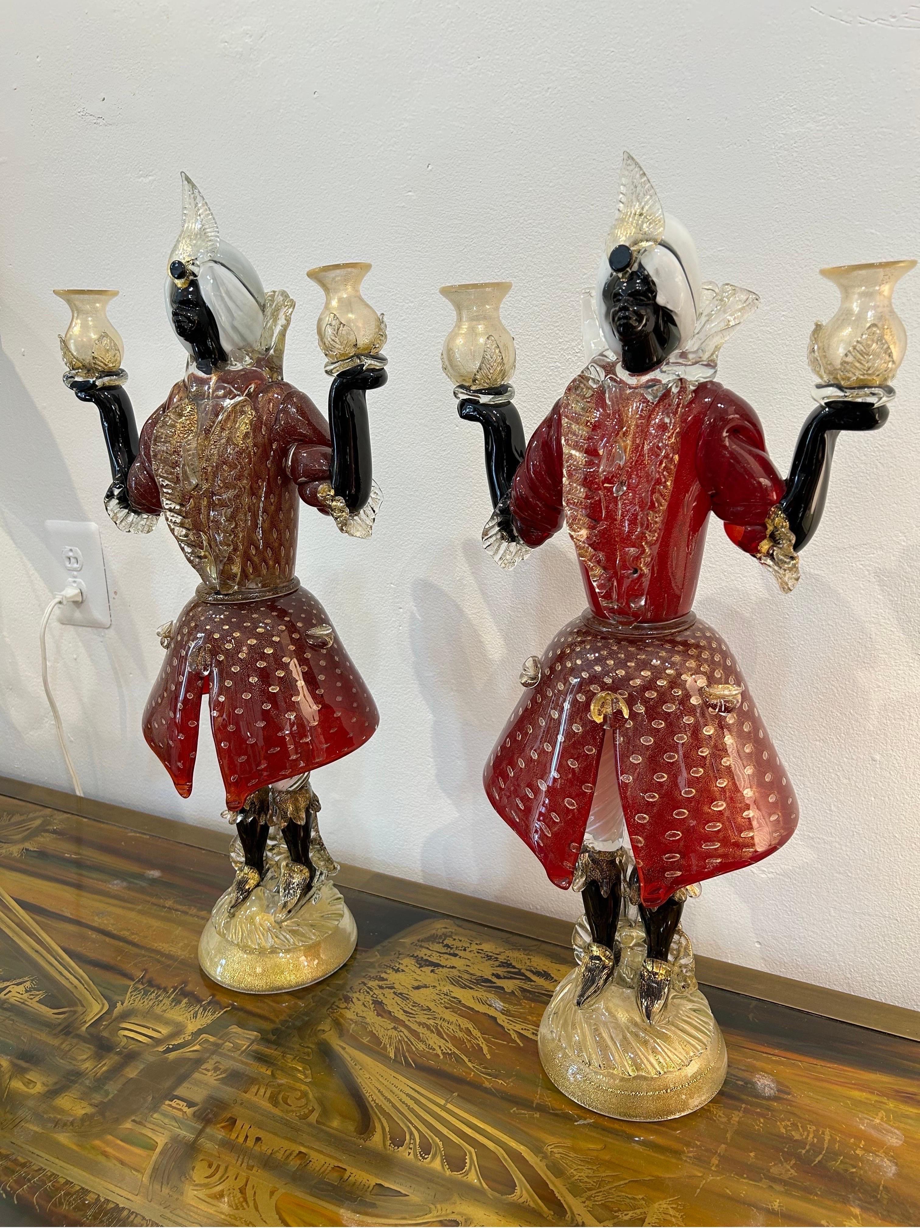 Very beautiful pair of highly decorated figural candleholders … ornately dressed figures in the 18th century Venmetiian ..Decorated in shades of red gold black and white glass… infused with bubbles and gold inclusions…Largest pair of figural