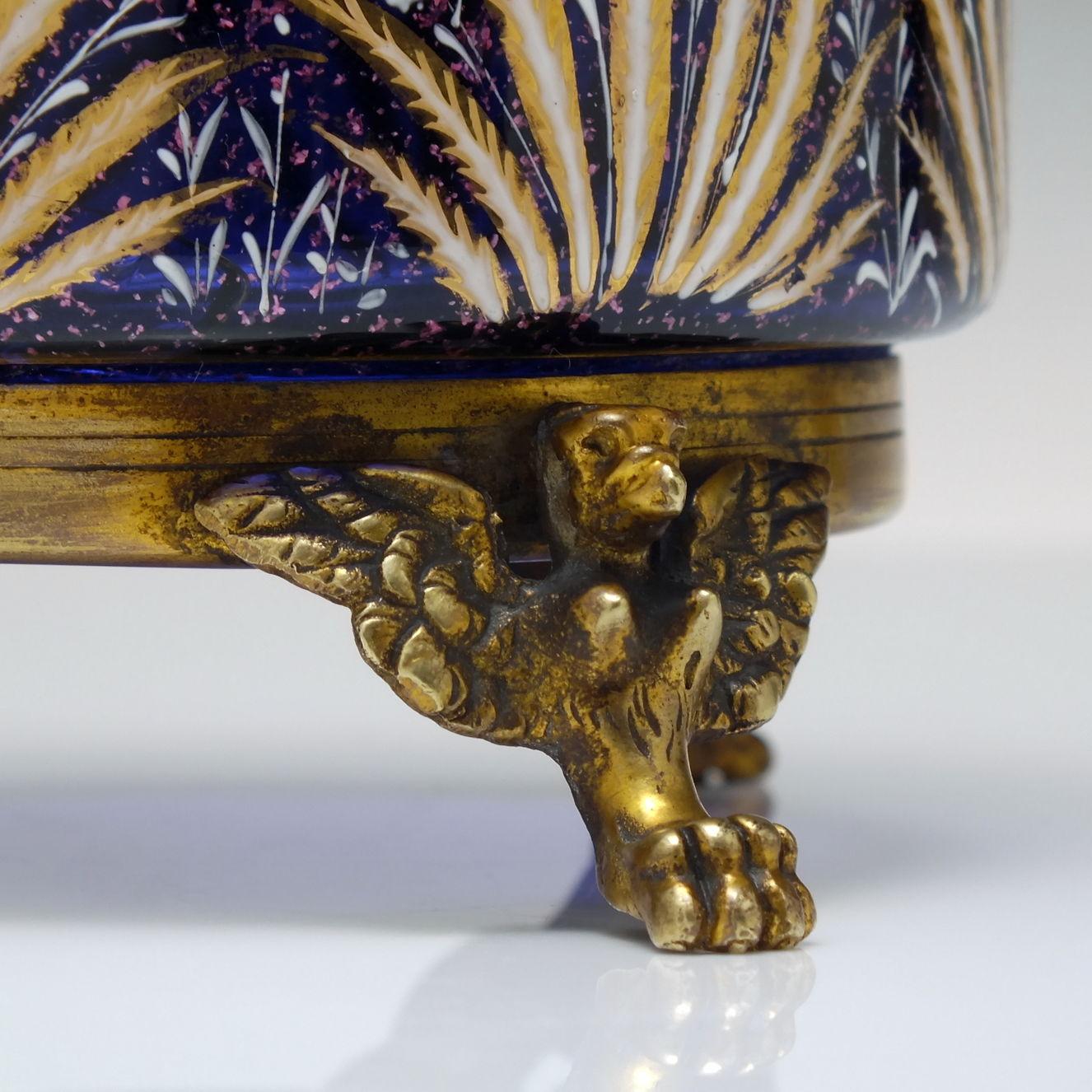 Technical Description 

A truly stunning pair of 19th-century glass vases hand-decorated in polychromatic enamels with grasses, flowers, and birds. Mounted on brass stands with three legs in the form of griffins. Blue glass with pink flecks when
