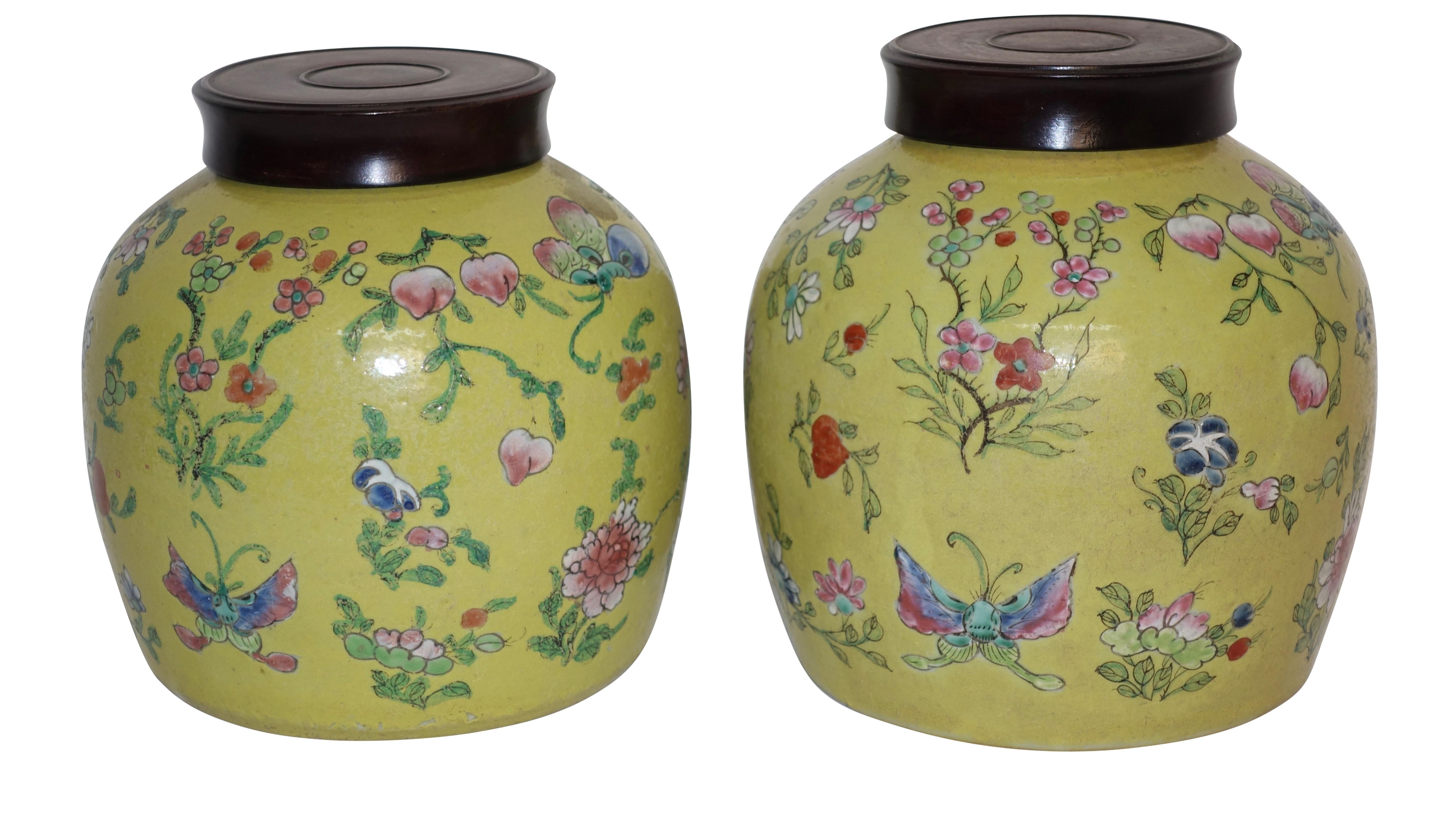 A pair of colorful Chinese jars with mustard color ground, having pink and blue flowers, pomegranates and butterflies, with hand carved wooden lids. China, Republic Period, early 20th century.