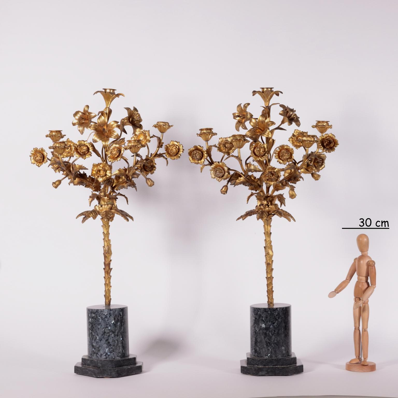 Pair of candelabra in gilded bronze. The marble base supports a palm from which starts a floral composition made of carnations and lilies to create a candelabra with five lights. Mercury gilding.