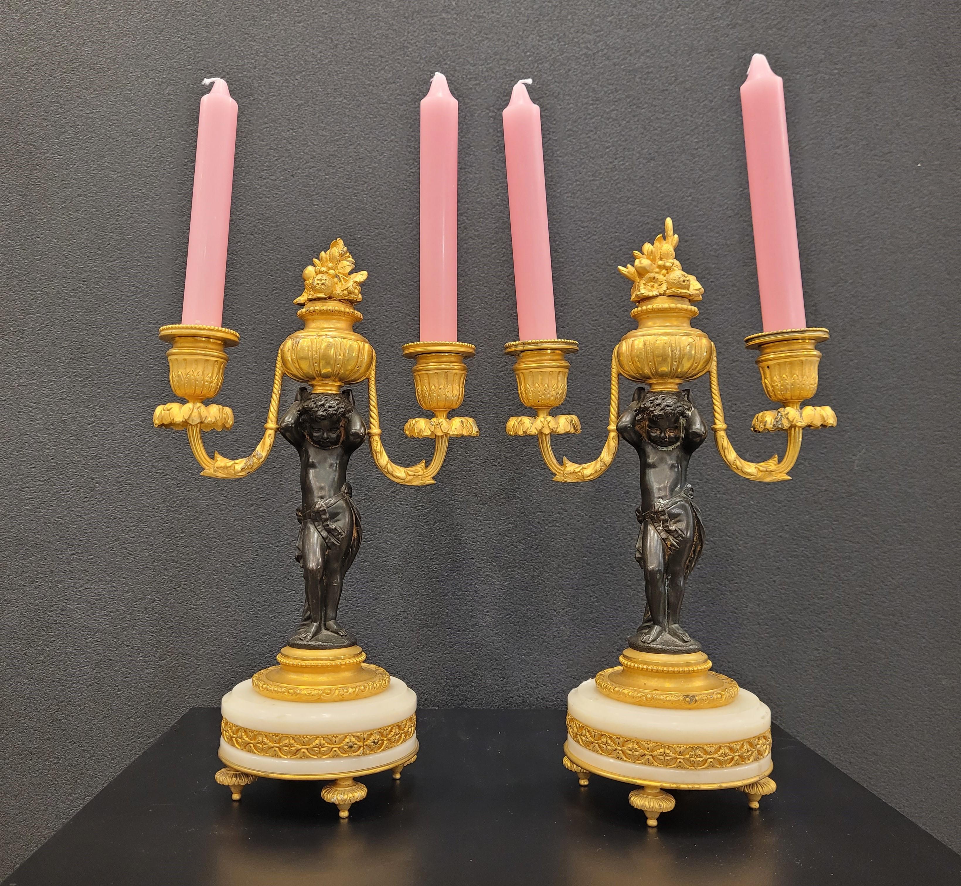 One of a kind and very Exquisite and refined pair of candelabras or cancelsticks in gilded bronze at the end of the 19th century in France. In each one, a delicate putto or cherub in patinated bronze with a dark finish, holding an ormolú basket with