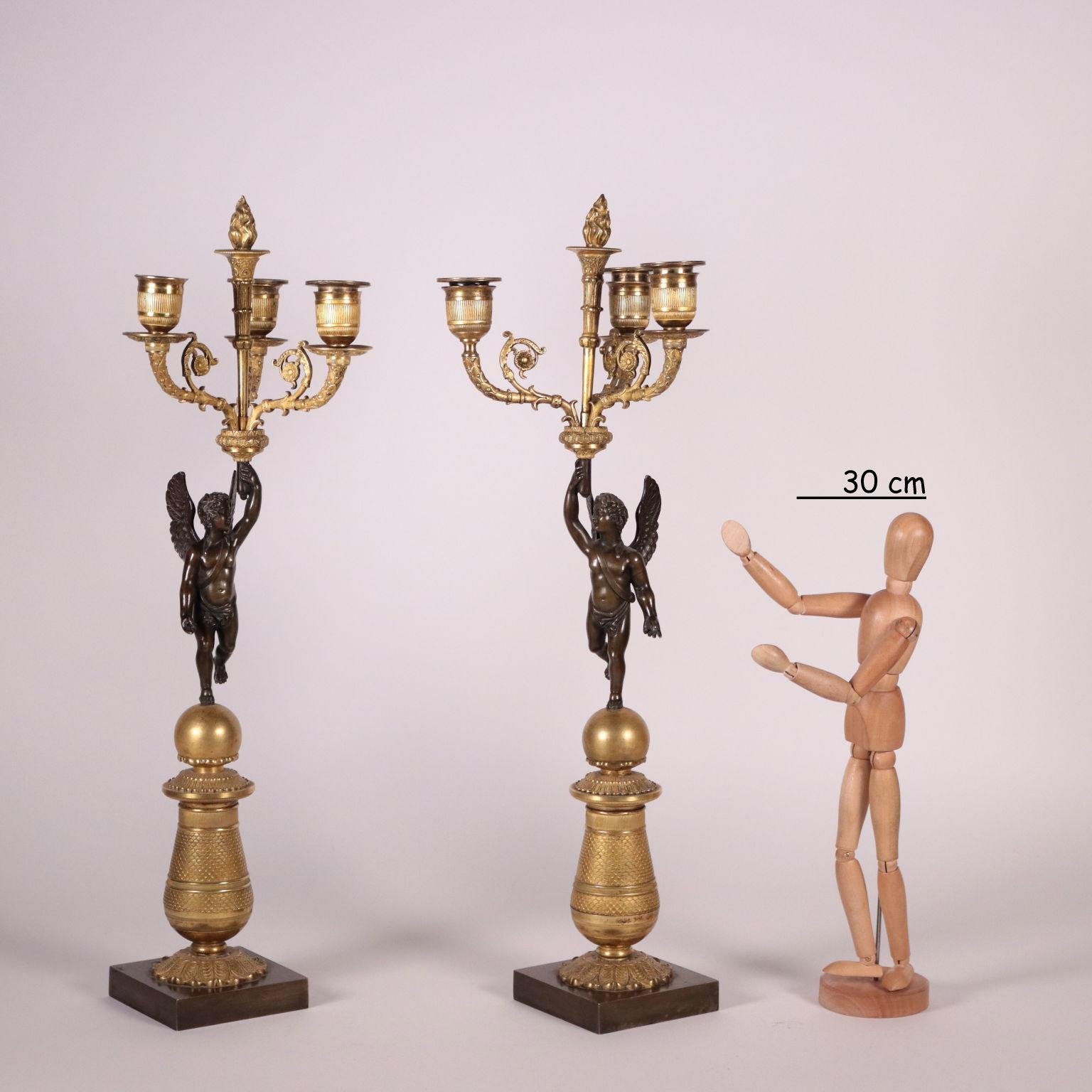 Pair of gilded bronze chandeliers with 3 lights. The arms are supported by a dark patined pronze putto that stands on a sphere and a vase-shaped plinth decorated with leafy elements and placed on a square base. Mercury gilding. 