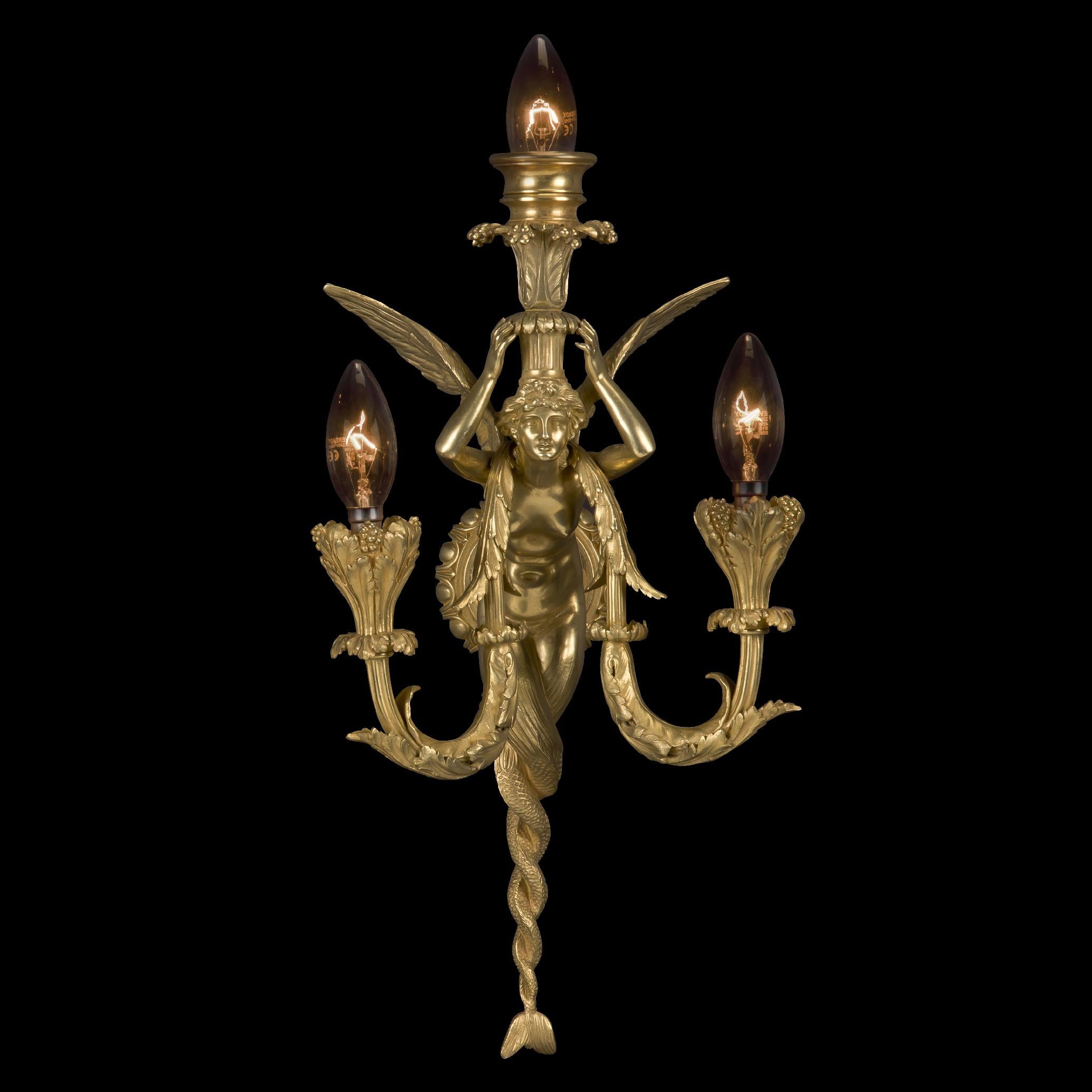 A fine pair of Napoléon III gilt-bronze three-light wall appliques, by Maison Millet.

Each applique is cast as a winged mermaid canephore figure supporting a palmette cast basket and issuing two acanthus wrapped scrolling candle branches