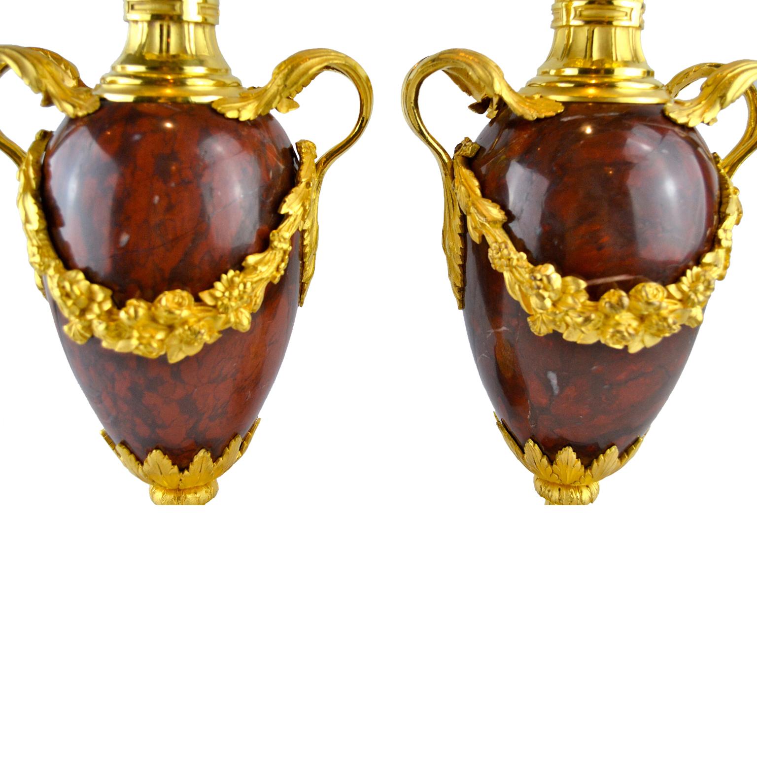 A fine pair of griotte (red), marble and gilded bronze casolettes in the Louis XVI style. The ovoid red marble body is decorated with gilt bronze handles joining gilt floral garlands across the front and back. The tapering bottom of the 'urn' is