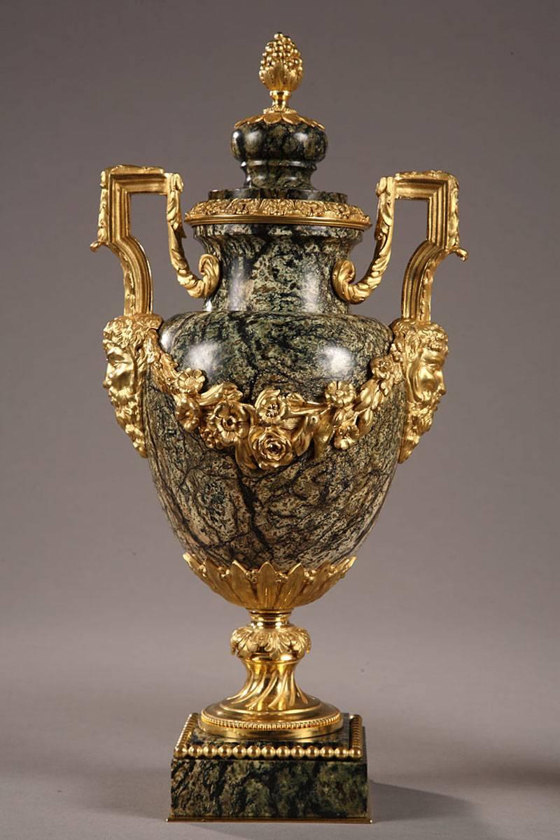 Pair of large, green marble vases with ormolu mounts and two gilt bronze handles. The handles are richly decorated with foliage and meet the body of the vases in the form of a bearded head. Flowery ormolu garlands wraparound the body of the vase to