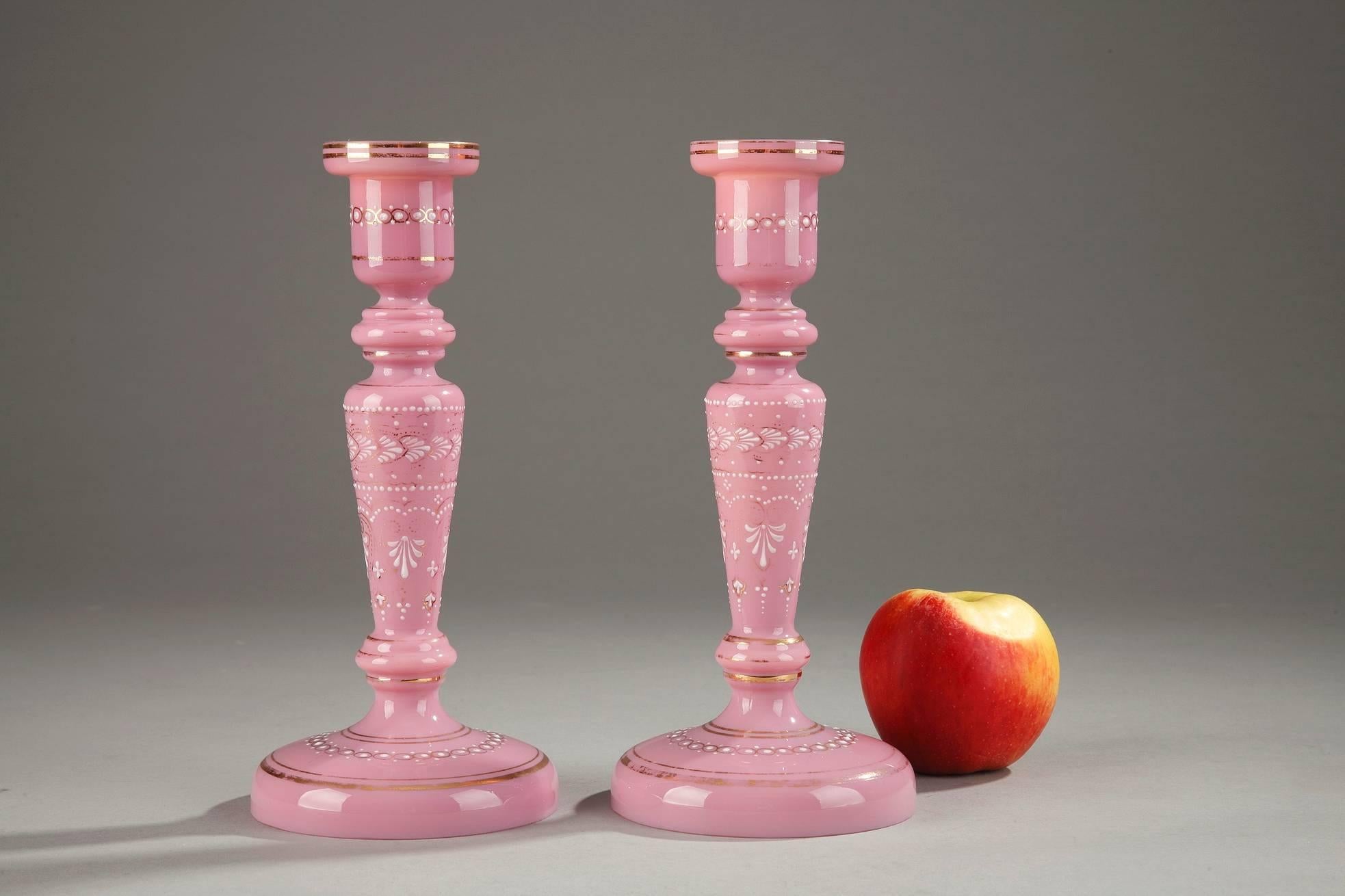 Pair of pink opaline candlesticks featuring white enamel palmettes, small dots and floral motifs. Gold bands highlight the enamel as well as the socket, shaft and base of the candlesticks. This ensemble gives the impression of a successful imitation