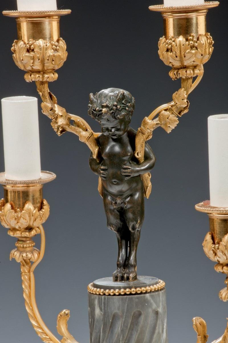 A pair of Napoleon III six-light candelabra
each with a young faun in bronze holding two ormolu candle branches entwined with vine leaves set upon stop fluted grey marble columns which support four further candle branches, all on square plinths and