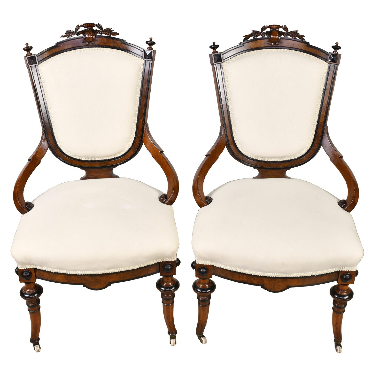 A beautiful pair of Napoleon III armchairs with walnut frame with burled walnut and ebonized details. Shield-back has carved laurel leaves with a cartouche over the crest rail with finials on the corners. Chairs have an upholstered back and seat,