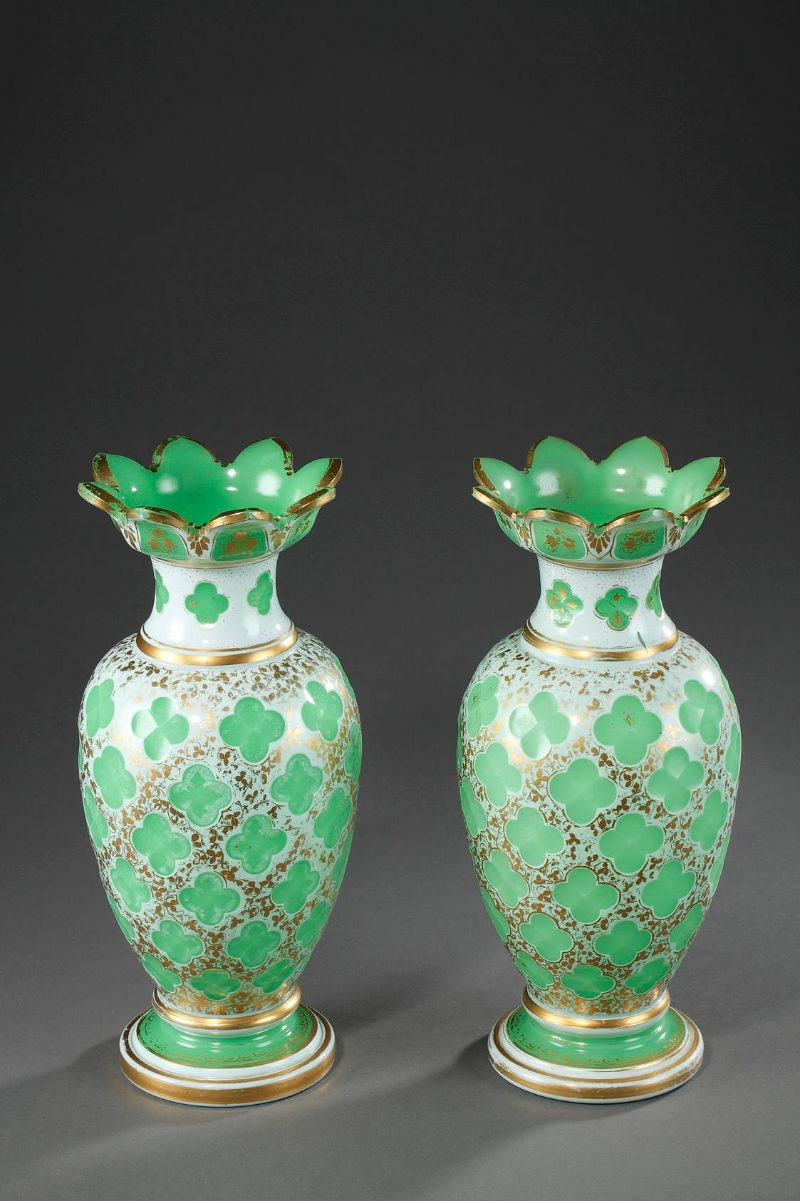 Pair of baluster-shaped decorative vases in opaline overlay with wide, petal-shaped rims. They are richly decorated with green, four-leaf clovers on a background highlighted with gilded, flowery garlands. The foot, heel, collar, and rim are