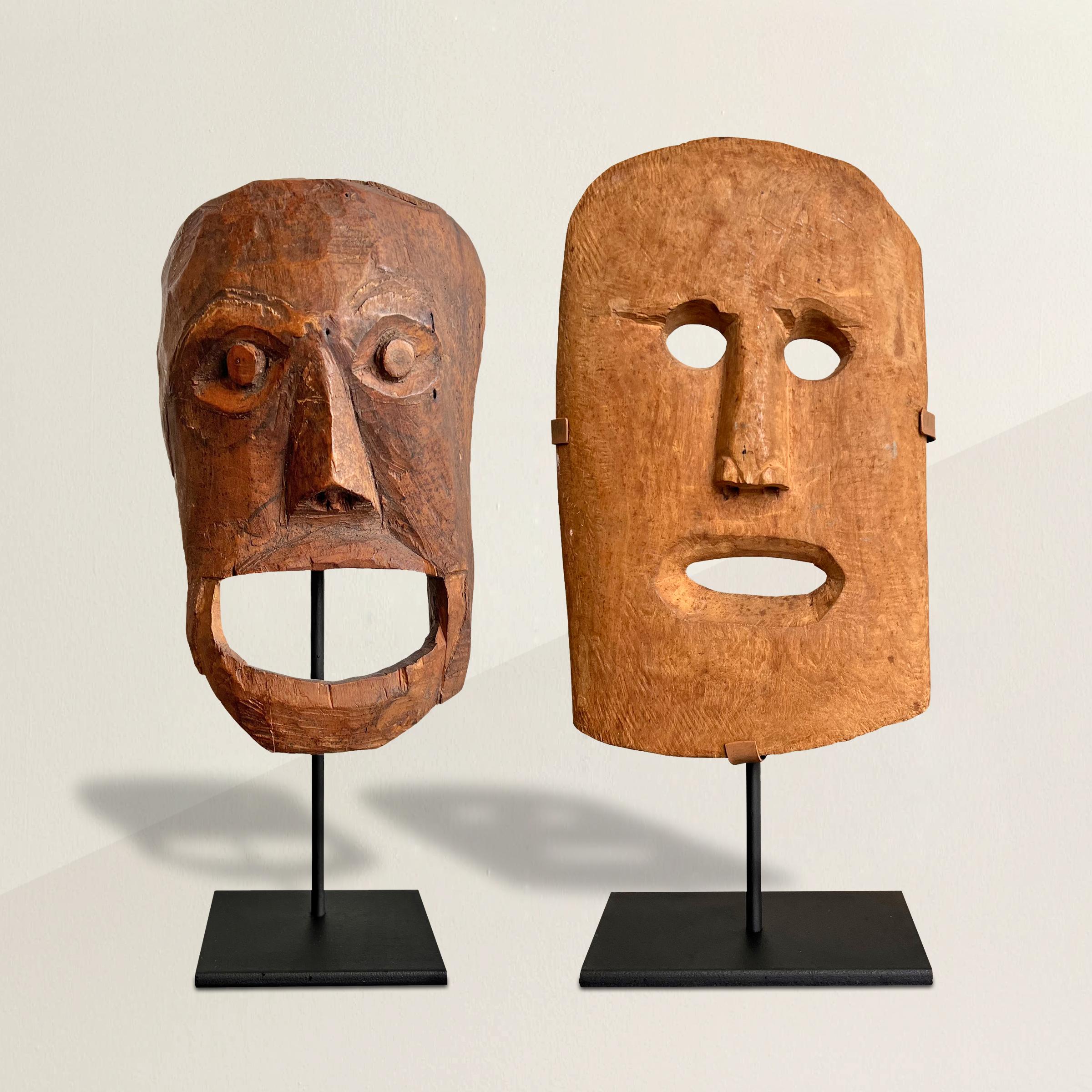 A striking set of two early 20th century Native American carved wood masks on custom steel mounts. The darker mask is inscribed in pencil on the back, 