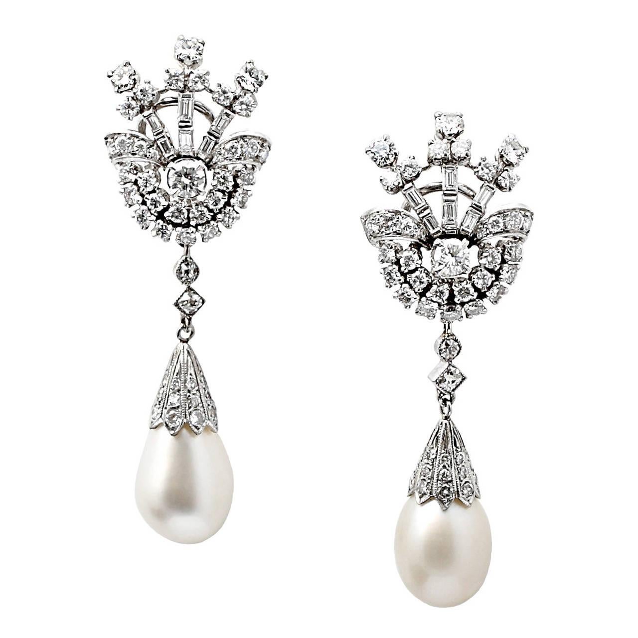 A magnificent and classic pair of two white, drop shape natural, saltwater pearls weighing 10.76 ct each, suspending from a single-cut diamond-set cap with a spray of three rows of channel-set baguettes accented with a cluster and ribbon of round