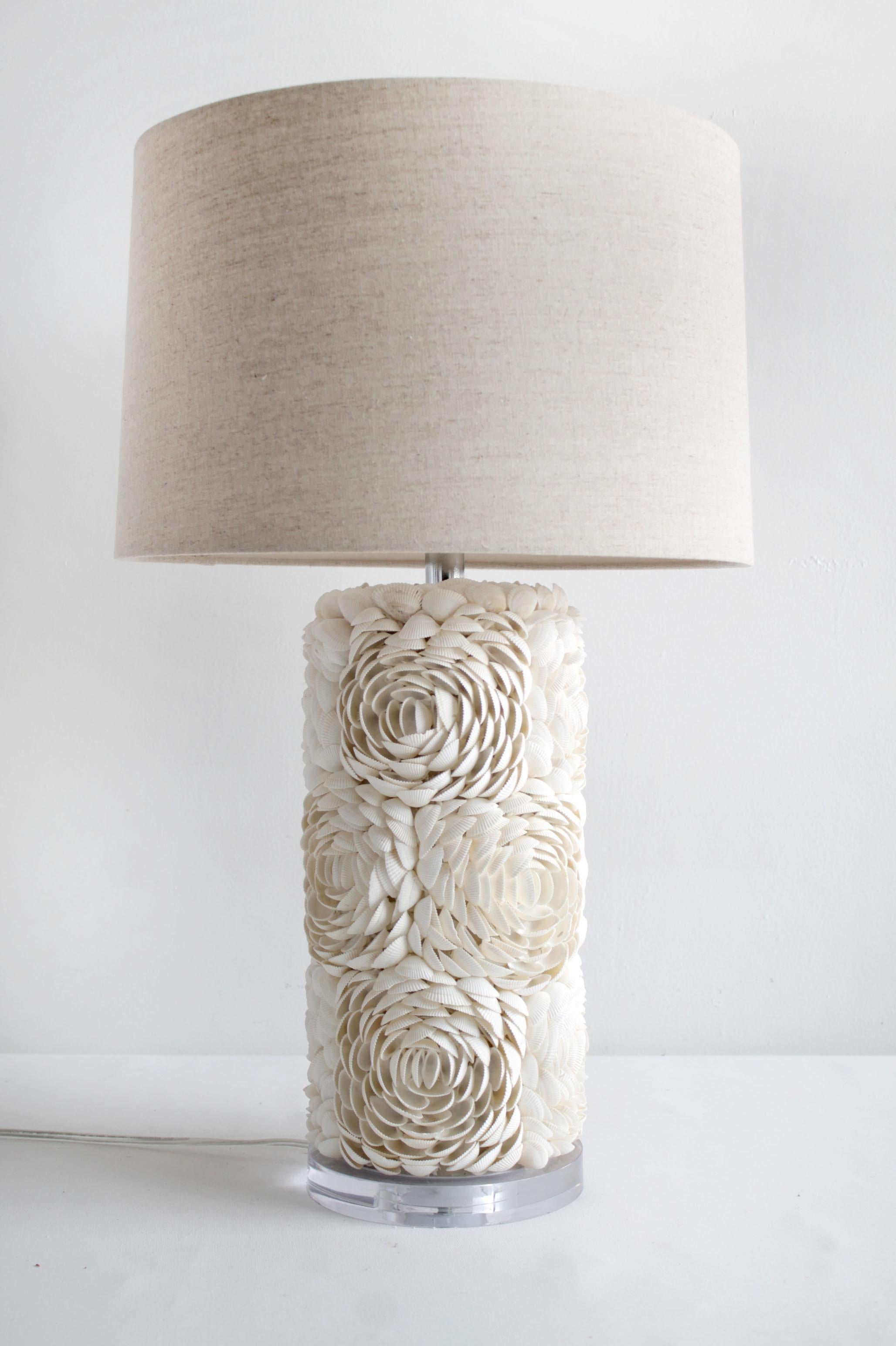 Pair of natural sea shell lamps with linen shades
White shells create a cup of rose clusters around the cylinder lamps. The base is a clear Lucite, with 3 way switch, standard US Plug, and natural linen shades.
Measures: 7