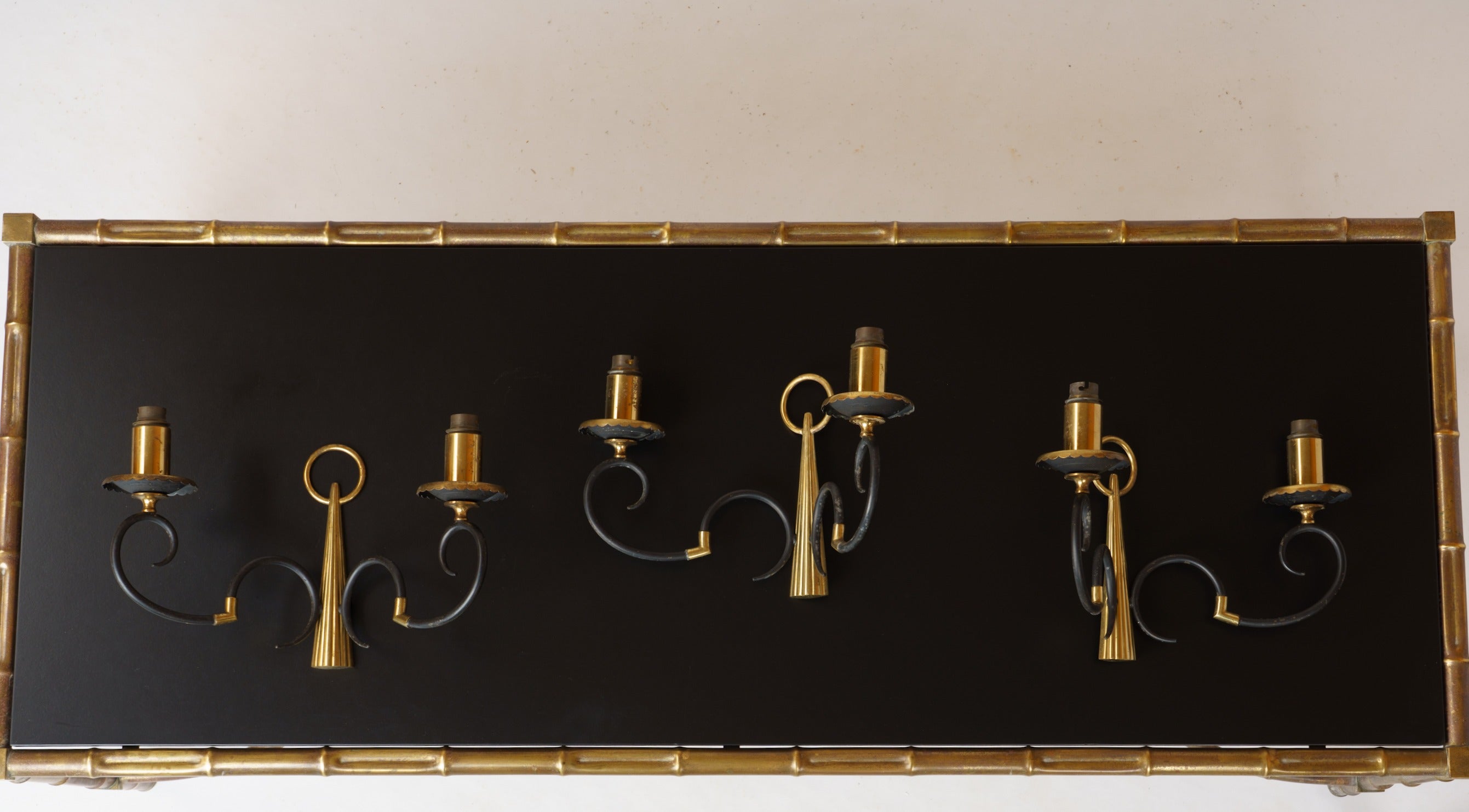 Una coppia di applique in stile neoclassico (la terza disponibile) realizzate negli anni '60 da Maison Arlus, un'azienda francese di illuminazione.
Due bracci luminosi a forma di doppio gancio rovesciato uniti da un pezzo di metallo dorato. Si