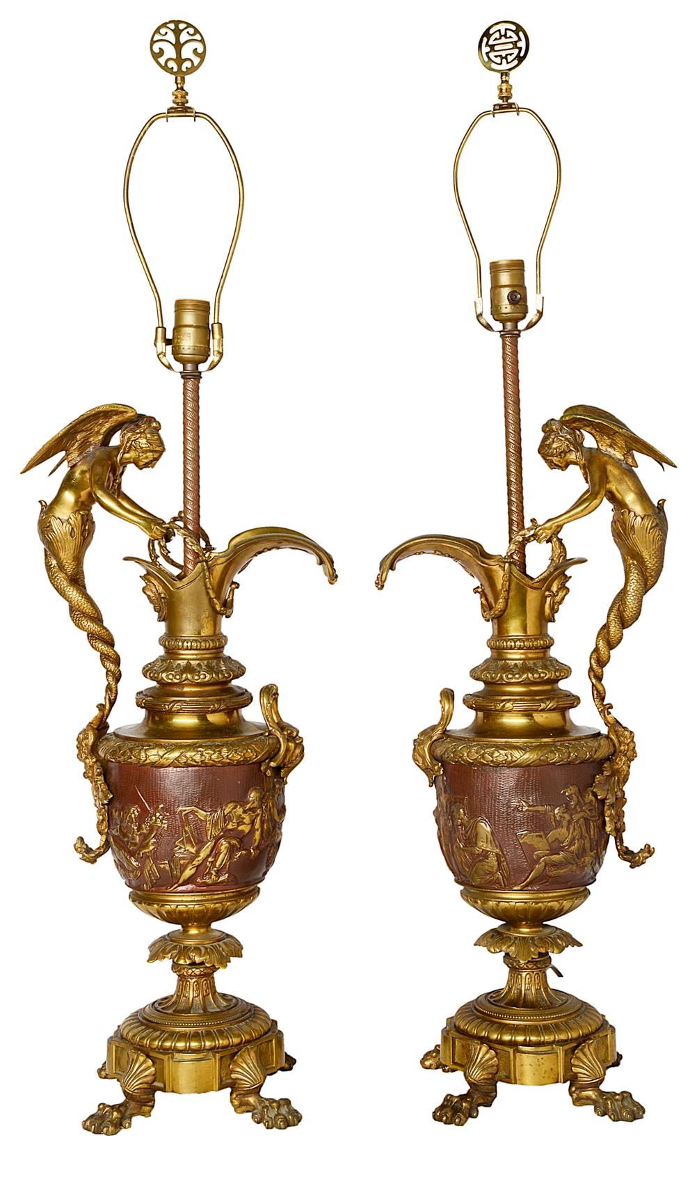 A good quality pair of late 19th century neoclassical bronze and ormolu ewer lamps. Each with wonderful winged mermaid like handles, mythical masks and classical scenes to the central panel, raised on foliate and shell decorated bases with claw feet.