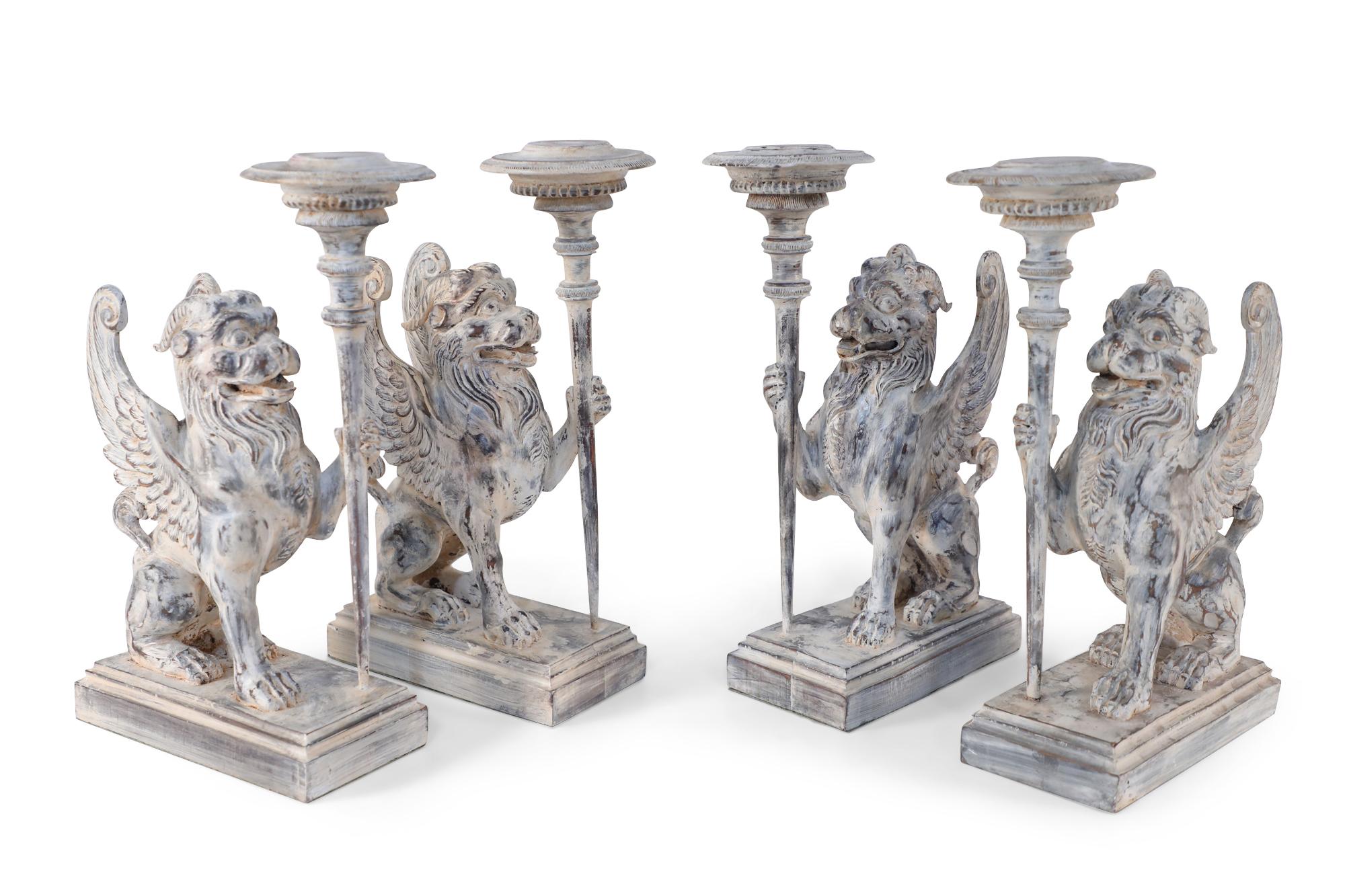 Pair of neoclassical style mythological carved wooden candle holders / bookends in the shape of chimeras holding a candle stick in one hand on stepped rectangular wooden bases with a white washed finish.
