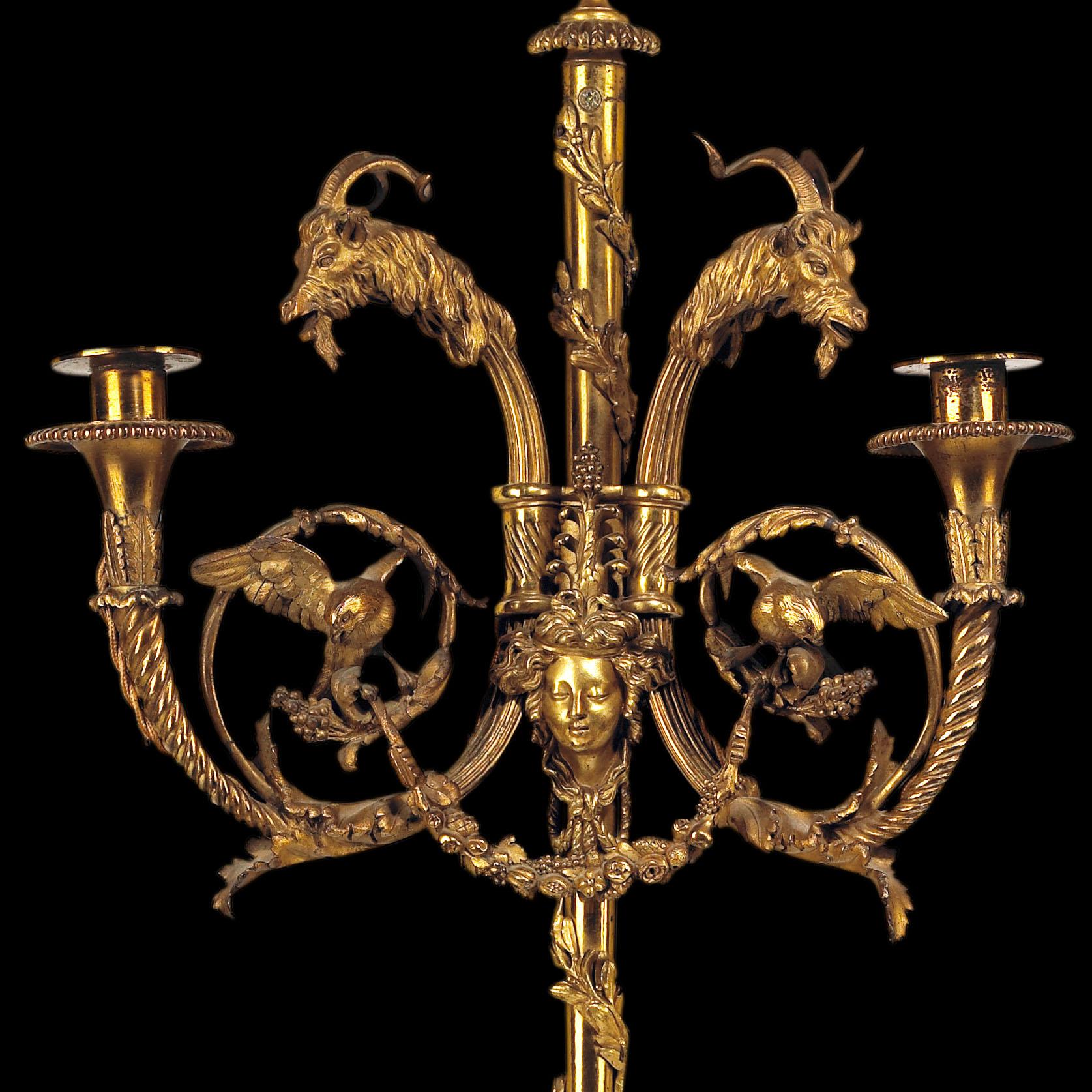 After a design by Jean-Louis Prieur. A pair of two-light wall appliques, the central canon barrel shaft with detailed pine cone finial wrapped in laurel leaves and supporting two curved arms with rams heads and foliate scroll work supporting finches