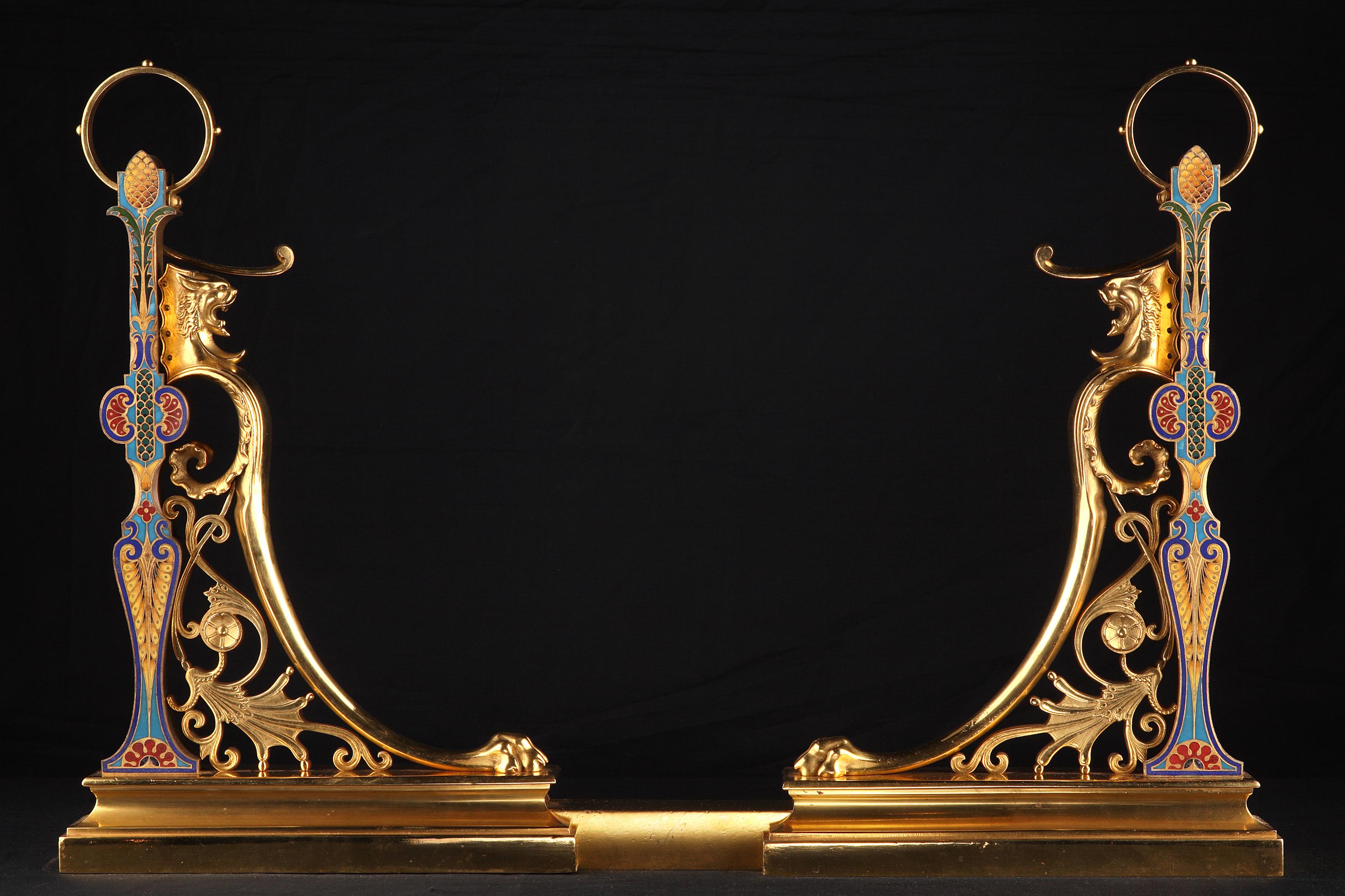 Measures: Height : 47 cm (18,5 in.) ; Width : 70 up to 96 cm (27,5 – 37,8 in.) ; Depth : 6 cm (2,3 in.)

A rare pair of square shaped andirons, made in gilded bronze and polychrome « champlevé » enamel. Designed in the Greek style with