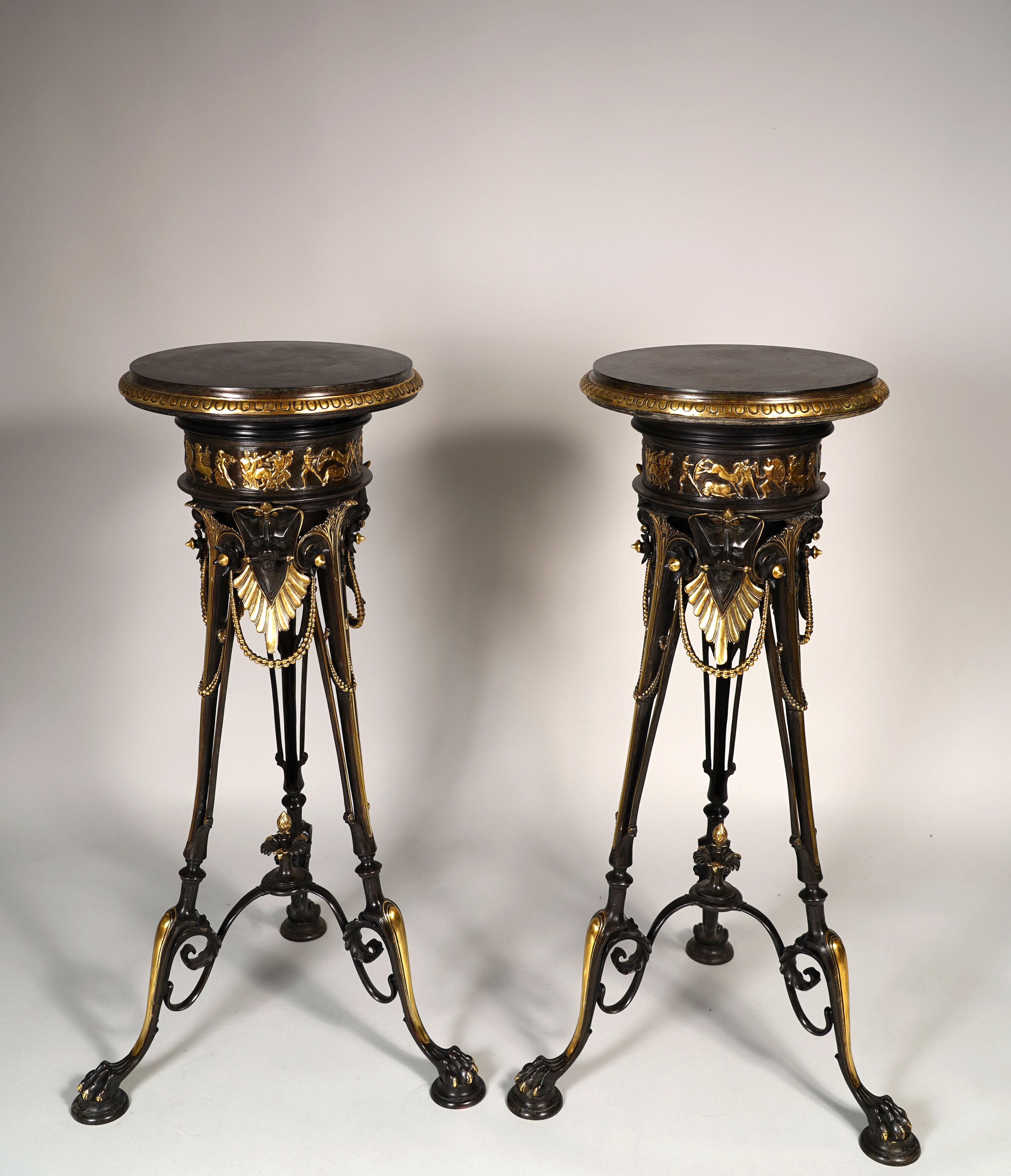 Pair of patinated and gilded bronze turntable pedestals with for each of them, three paw feet, headed by stylized lion muzzles, ornated with beaded chains and joined by a fine foliate stretcher. The belt is adorned by a banded frieze cast in