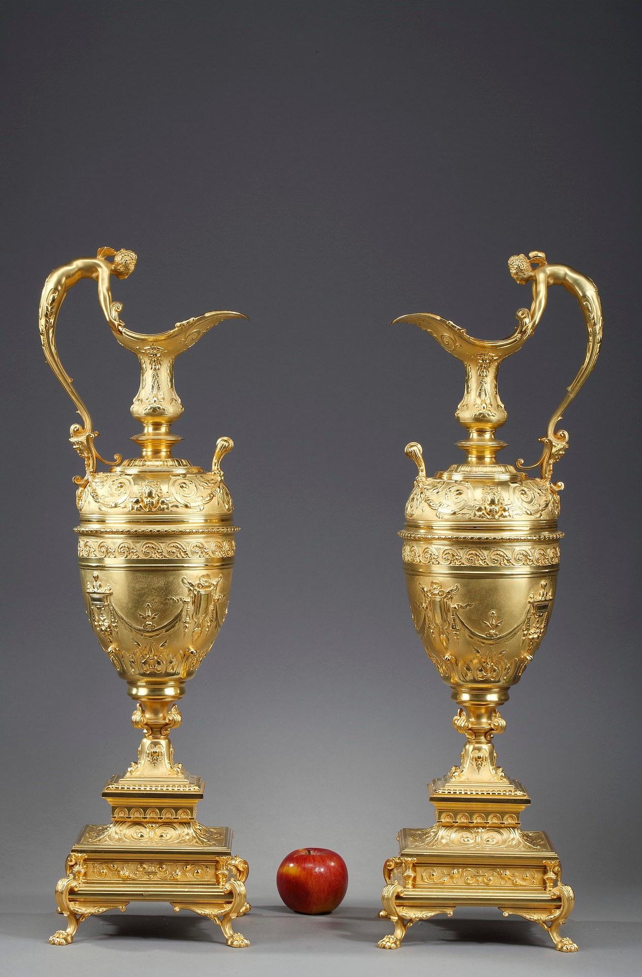 Large pair of neo-renaissance decorative ewers in gilt bronze richly decorated in relief. The central part is decorated with floral motifs, garlands, a frieze with scrolling motifs and two angels' heads. The neck is decorated with a frieze with