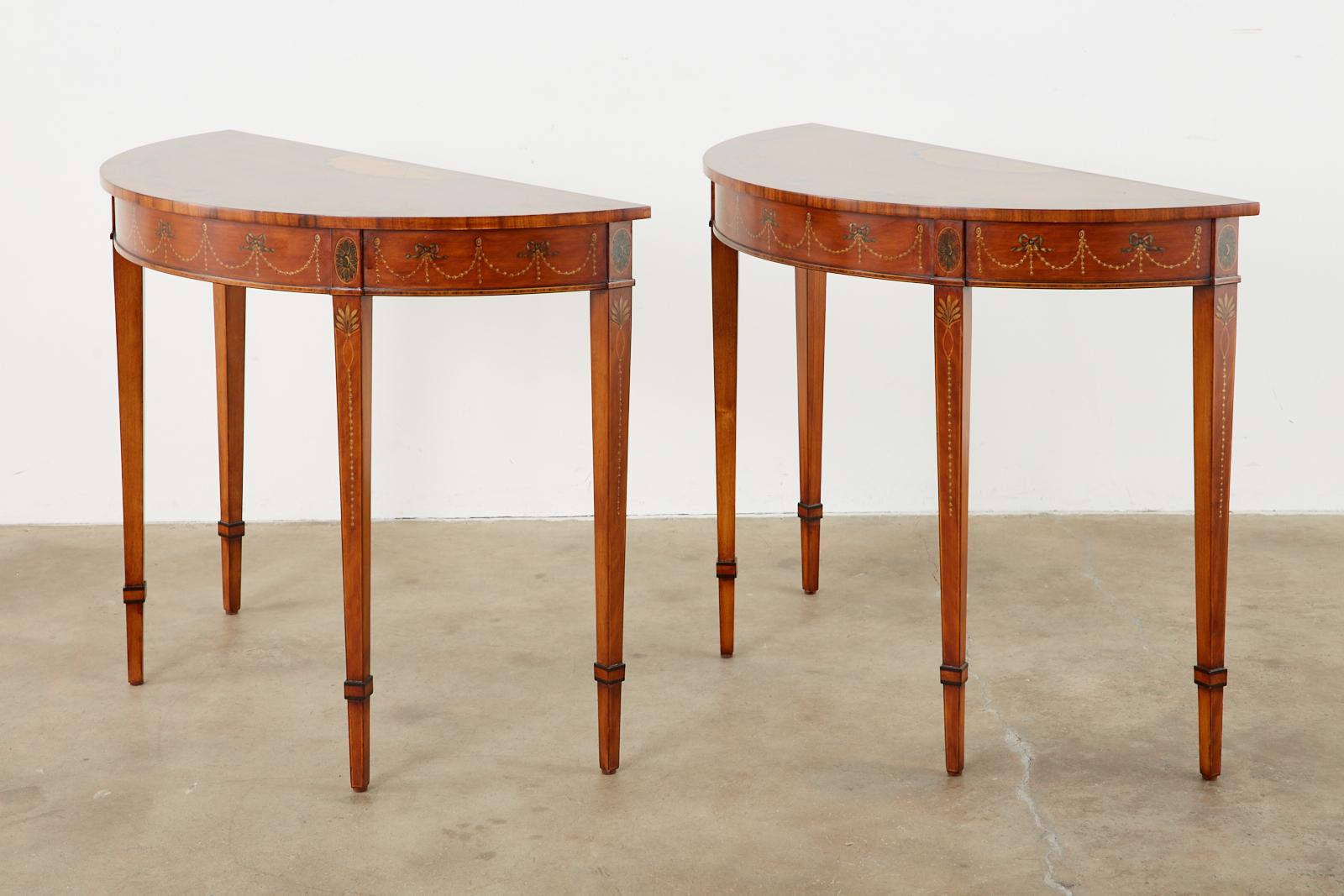 Brilliant pair of mahogany console or demilune tables produced by Schumacher in the 18th century neoclassical Adams taste. The beautifully veneered cases are embellished with thread inlay and satinwood then decorated with swags of floral garlands