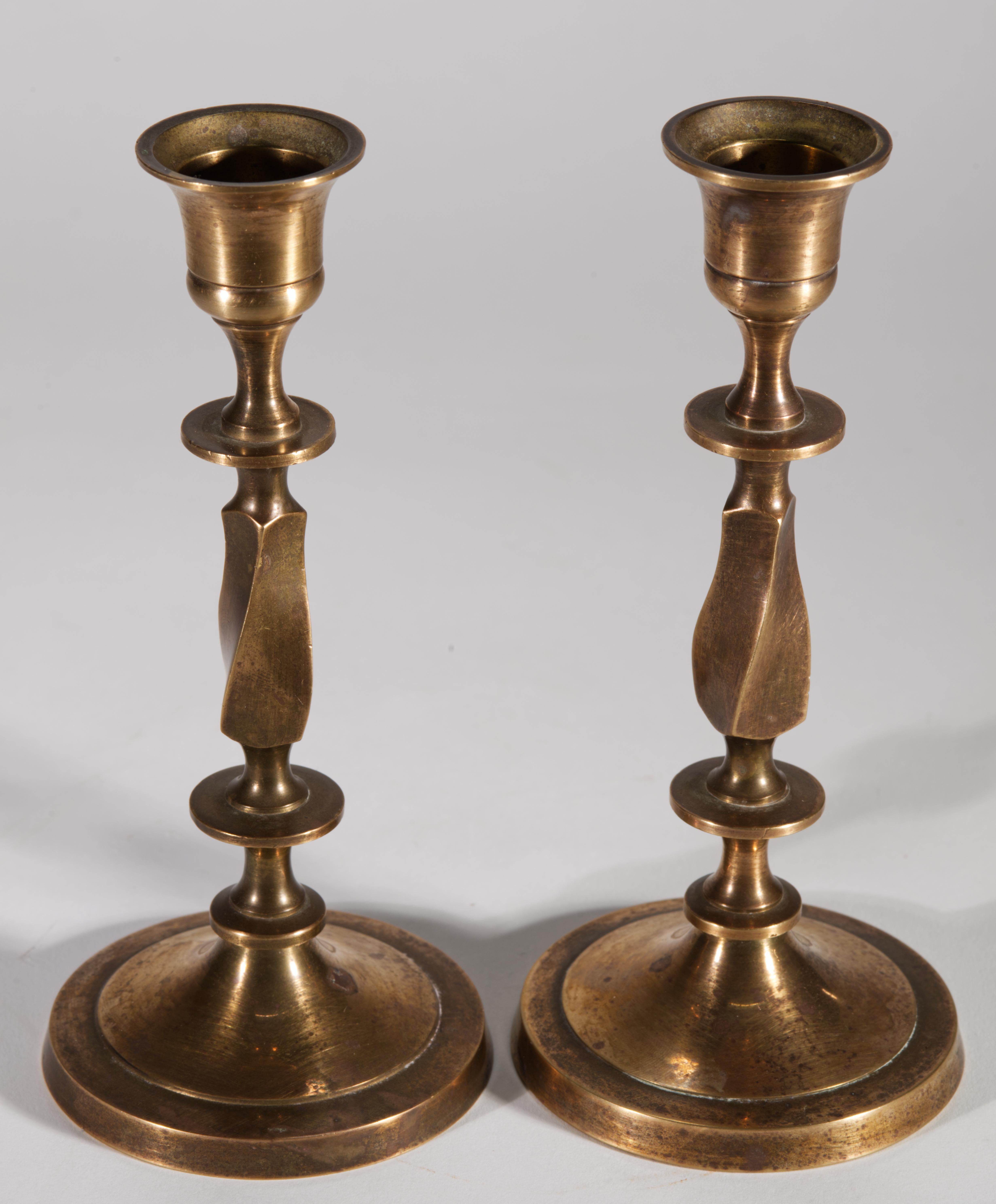 Coppia di candelieri neoclassici d'epoca in bronzo dall'elegante forma a balaustro con ampie basi circolari. I corpi scultorei con un elemento contorto sono sostenuti da basi rotonde a gradini che aggiungono stabilità a pezzi pesanti e