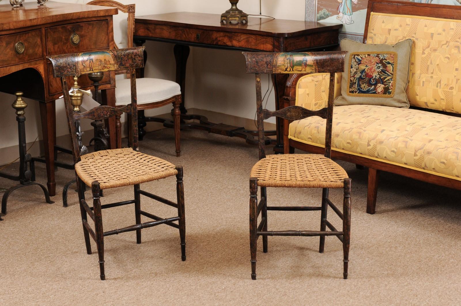 A pair of Neoclassical Black Painted Side Chairs with Woven Seats, Italy circa 1790. These period chairs feature rounded tapered legs and a unique individual figural painted scene at the top of each seat back.