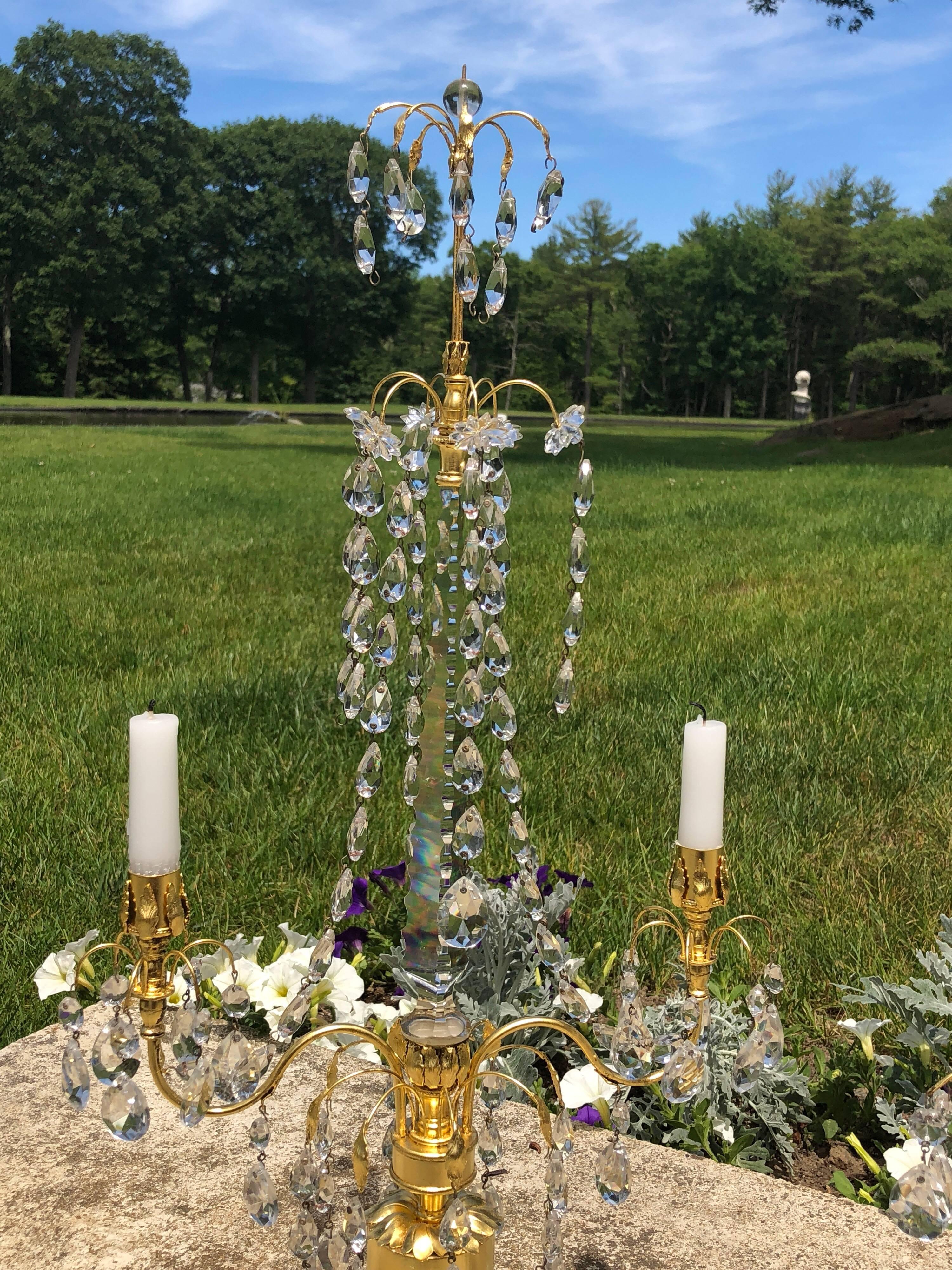 A beautiful pair of Swedish neoclassical Gustavian Style two-arm candelabra. The white marble base supports an ormolu adorned gilt wooden column out of which a crystal spike rises with teardrop crystal swags connecting to the arms on each side.